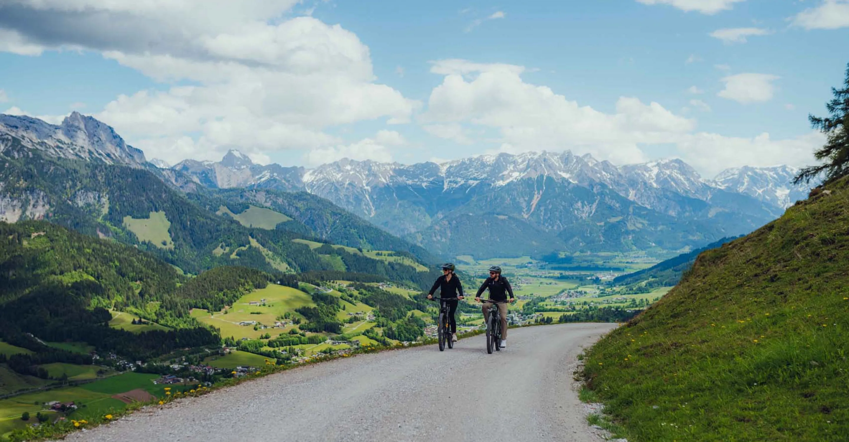Two cyclists on a path with mountains in the background