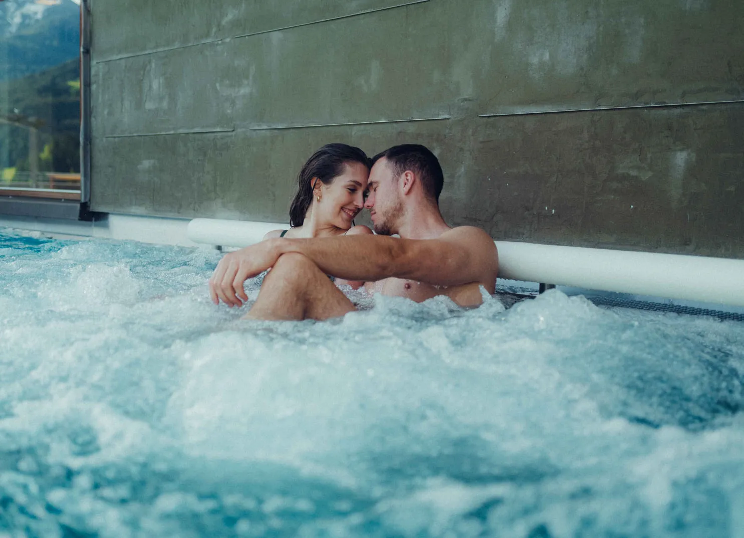 Couple relaxing in pool, surrounded by bubbles and water.