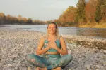 Frau meditiert am Fluss mit Kieseln und Bäumen