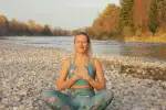 Frau meditiert an einem Fluss in der Natur