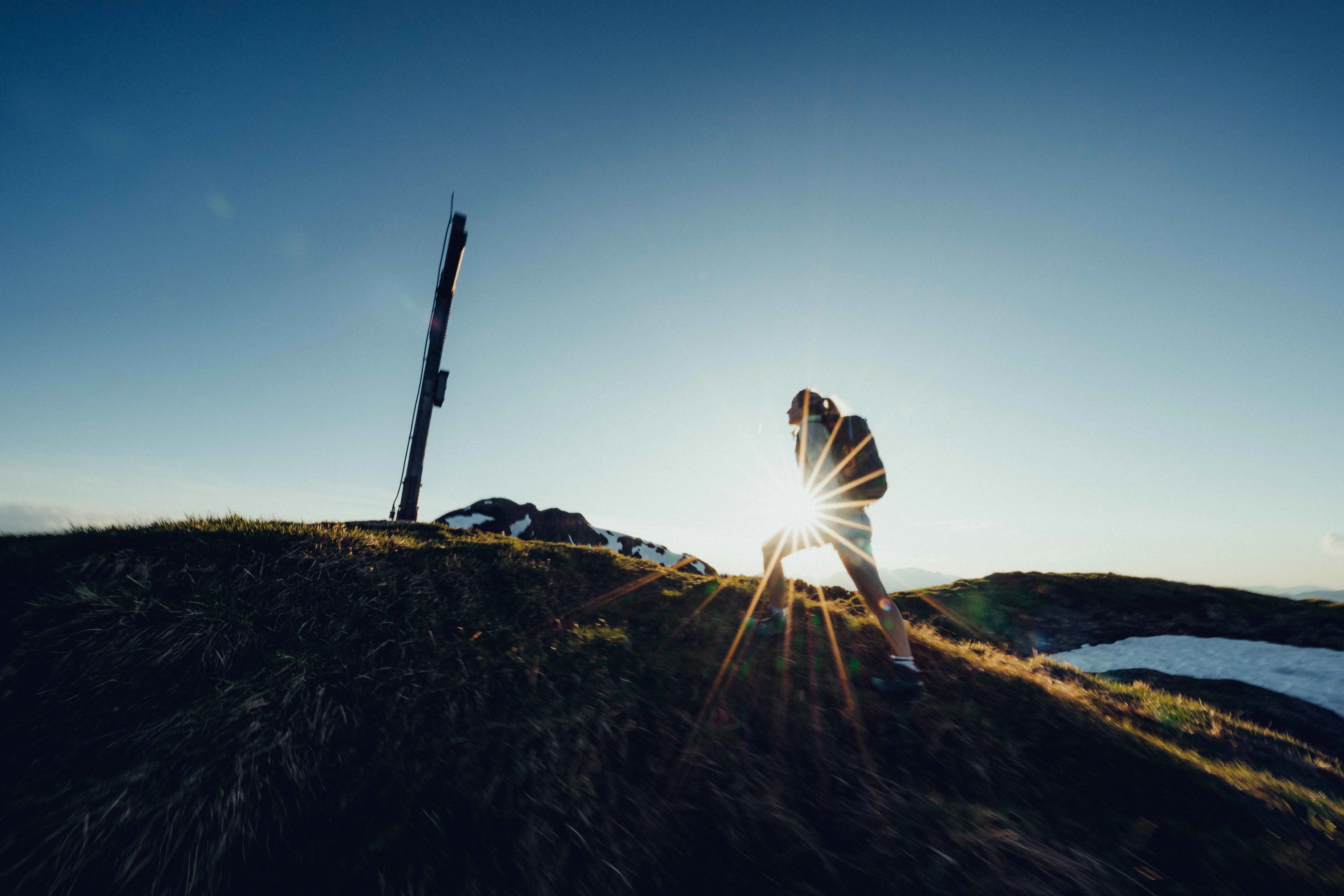 Person auf einem Hügel bei Sonnenuntergang, im Hintergrund ein Holz-Signal.