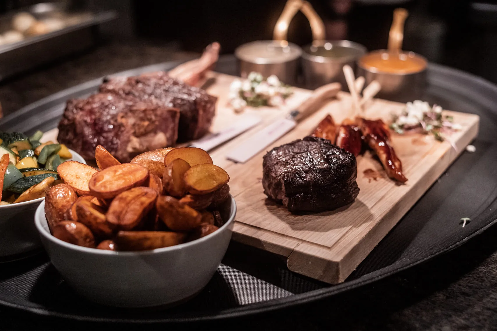 Platter with meat, potatoes, vegetables, and sauces on a serving tray