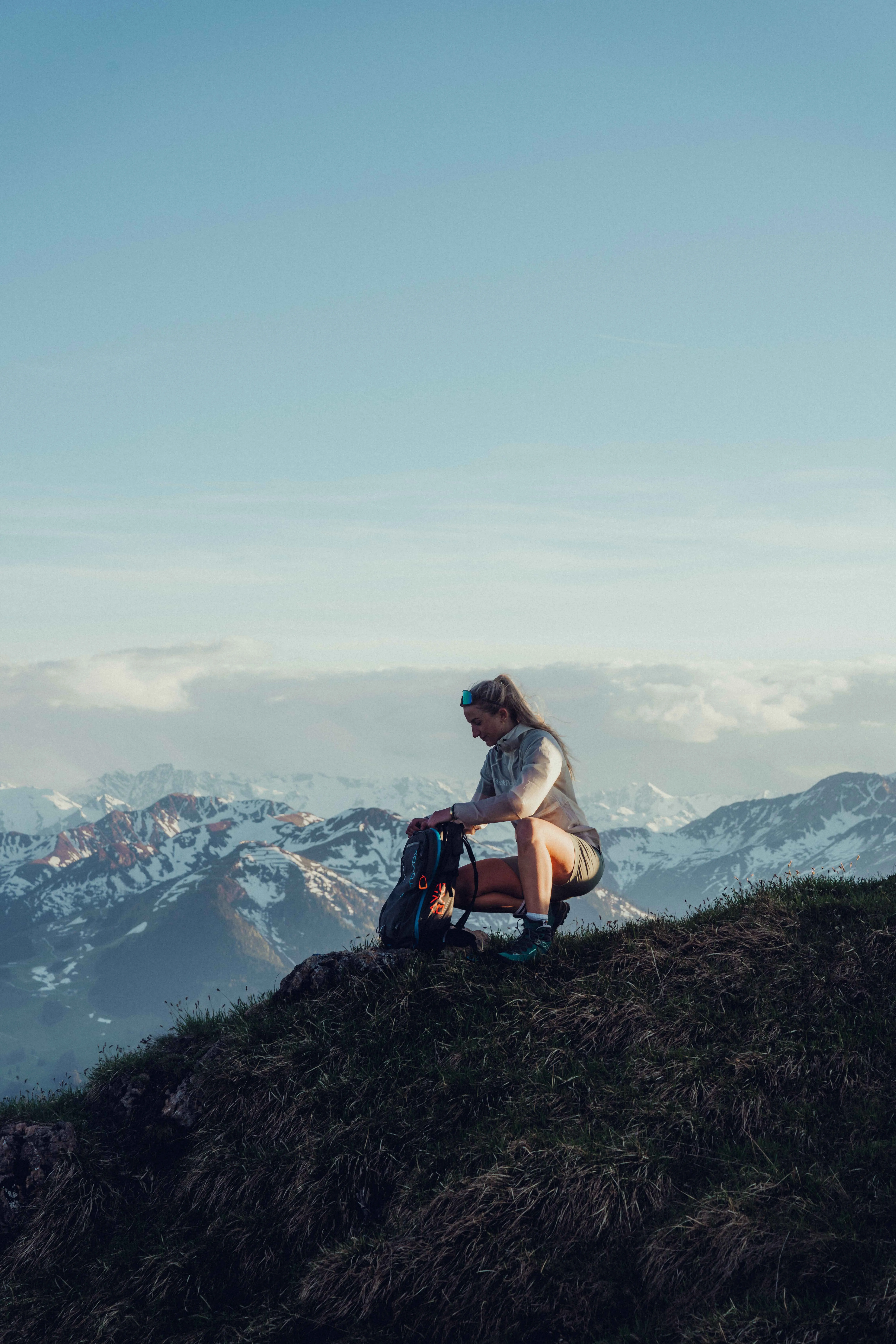 Person sitzt auf einem Hügel mit Blick auf bergige Landschaft.