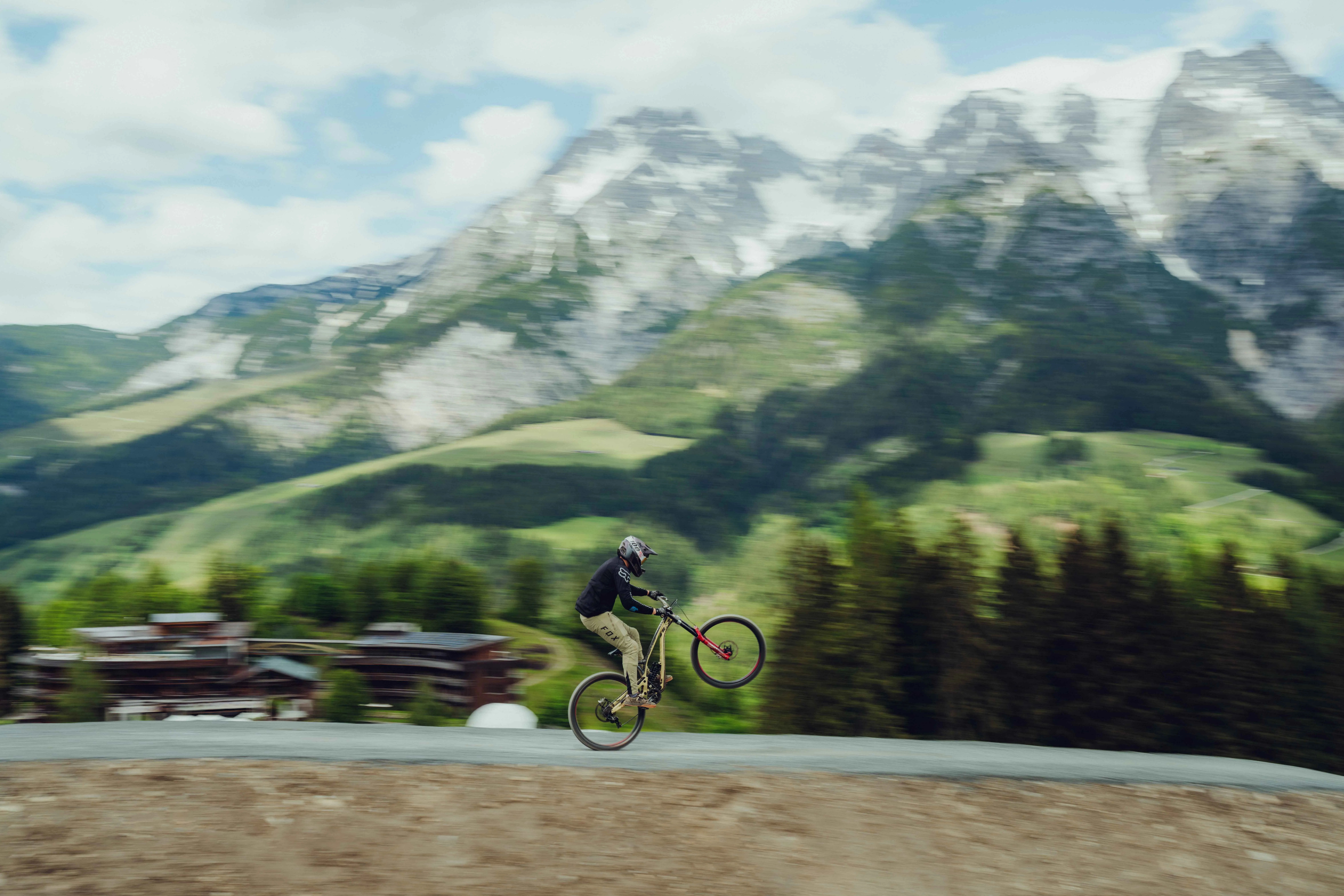 Radfahrer springt vor Berglandschaft mit Holzhotel im Hintergrund