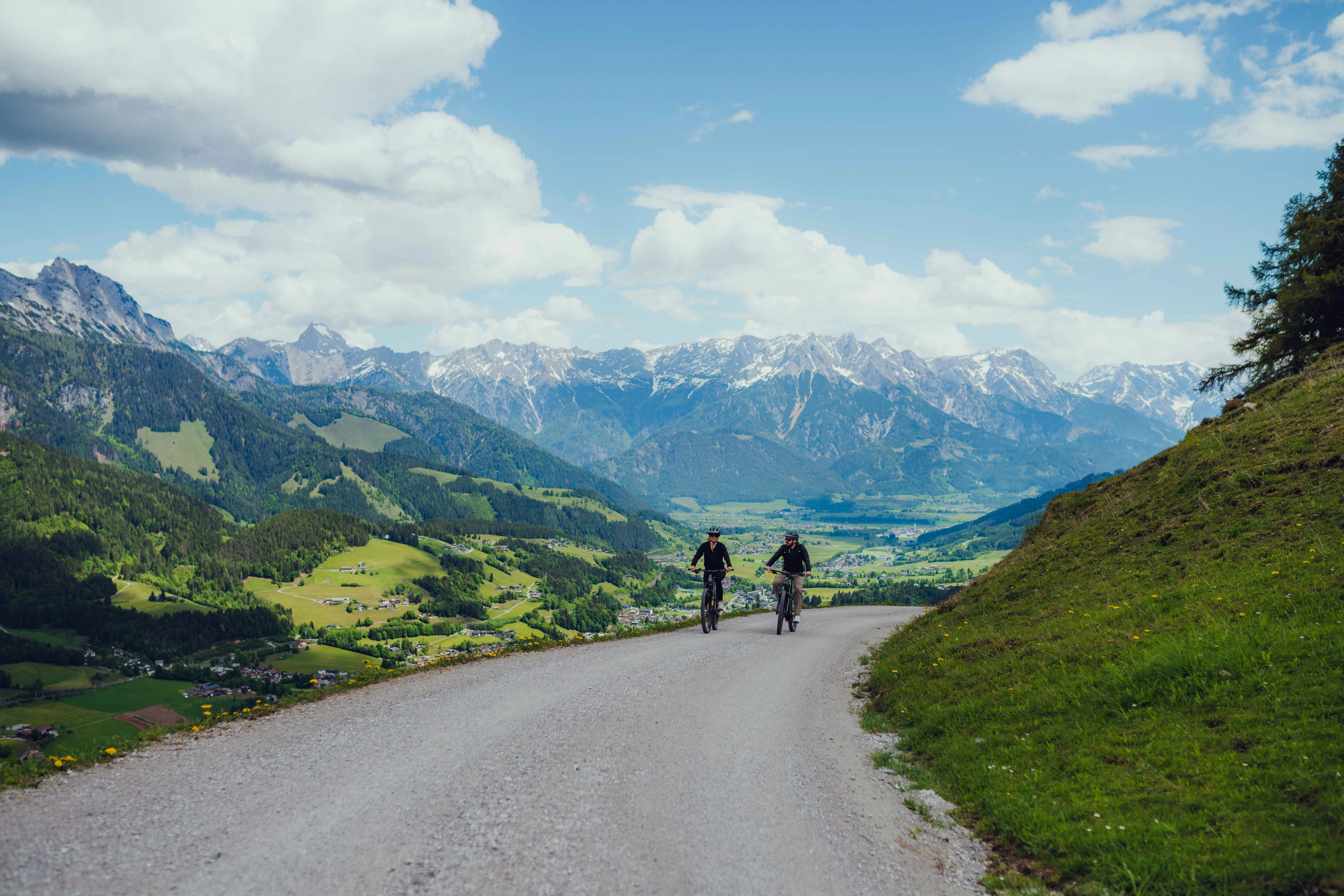 Zwei Radfahrer auf einem Schotterweg in Leogang mit Bergpanorama im Hintergrund.