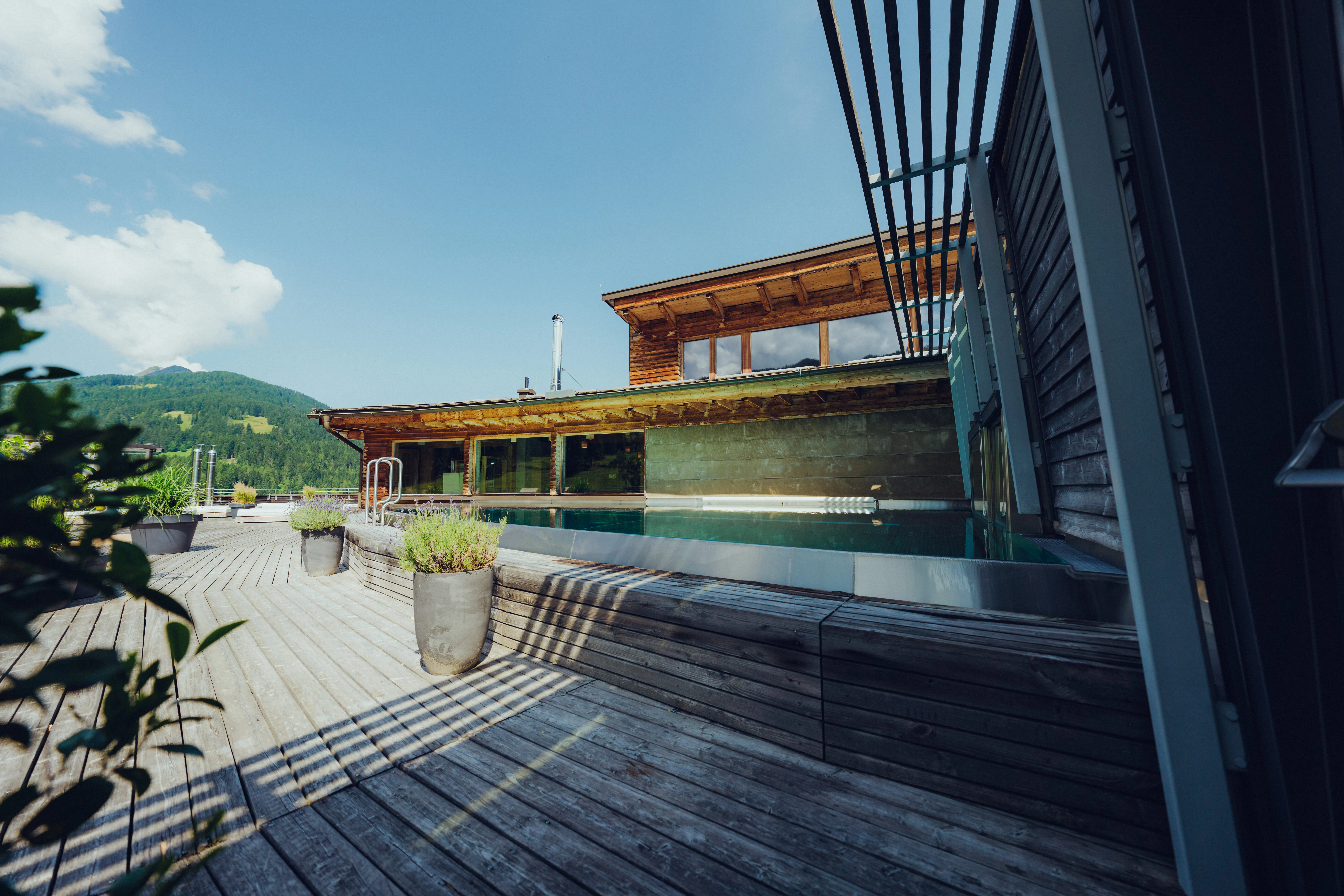 Wooden spa with pool and plants on a deck, mountains in the background.