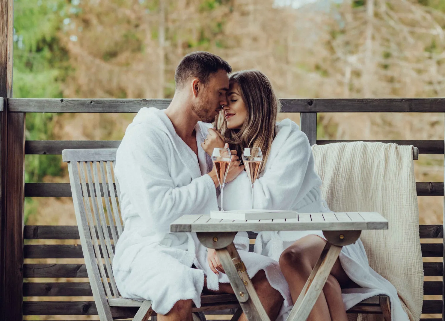 Paar in Bademänteln mit Cocktails auf der Terrasse des Holzhotels Forsthofalm