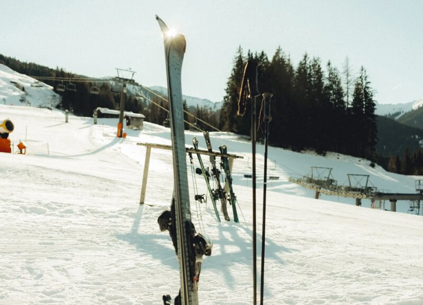 Schneebedecktes Skigebiet mit Skiern an einem Gestell und Bergen im Hintergrund