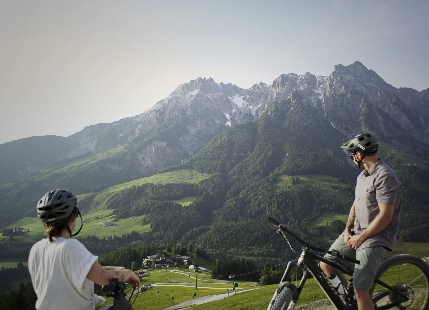 Zwei Radfahrer bewundern die Berglandschaft mit saftig grünen Tälern.
