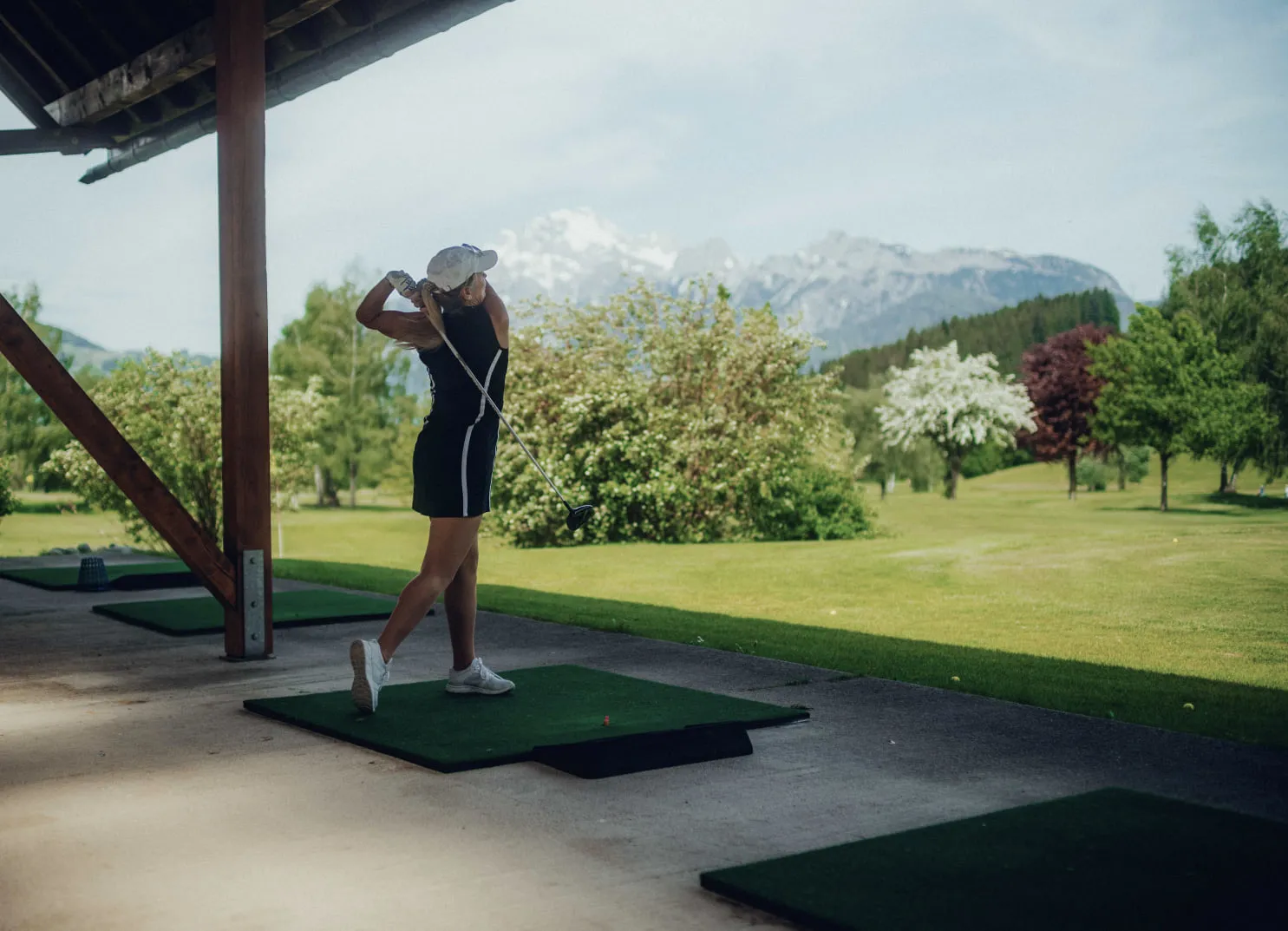 Dame beim Golfspielen auf einem Übungsplatz mit Bergen im Hintergrund