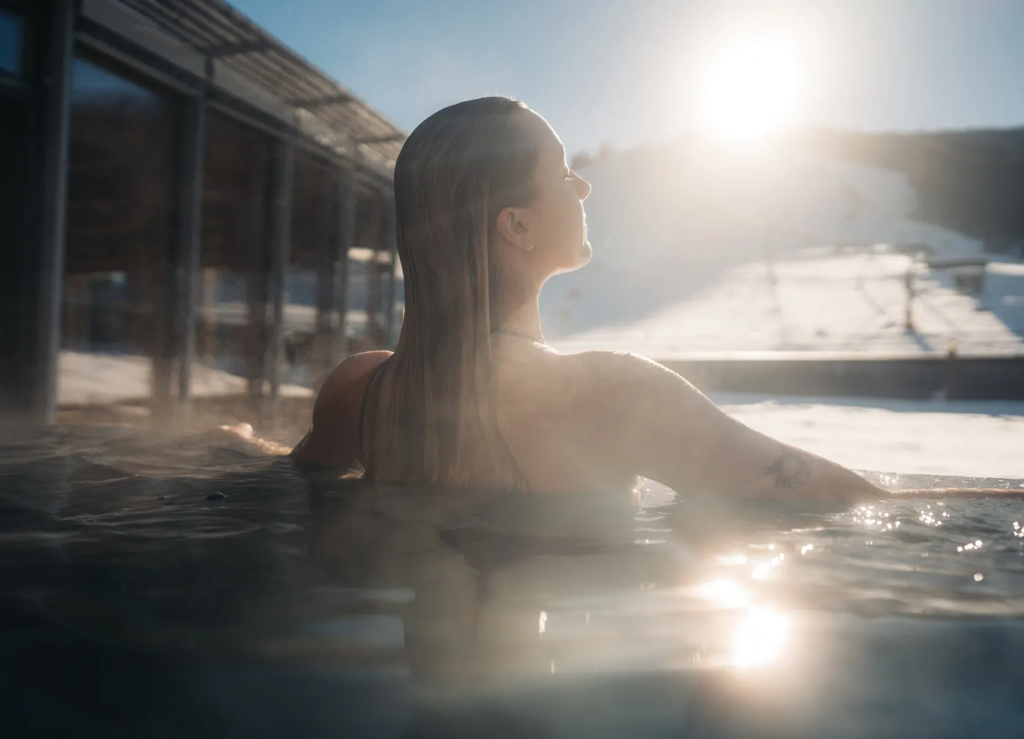 Woman in water with a view of a snowy slope and the sun
