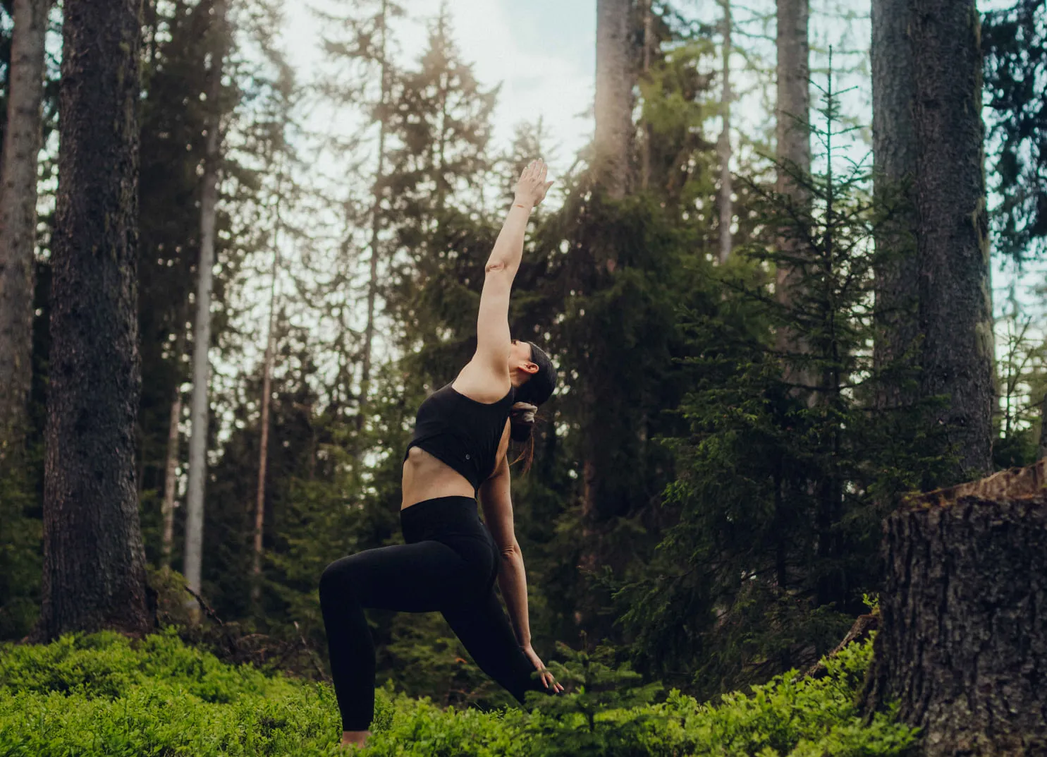Woman practicing yoga in a forest with trees and grass