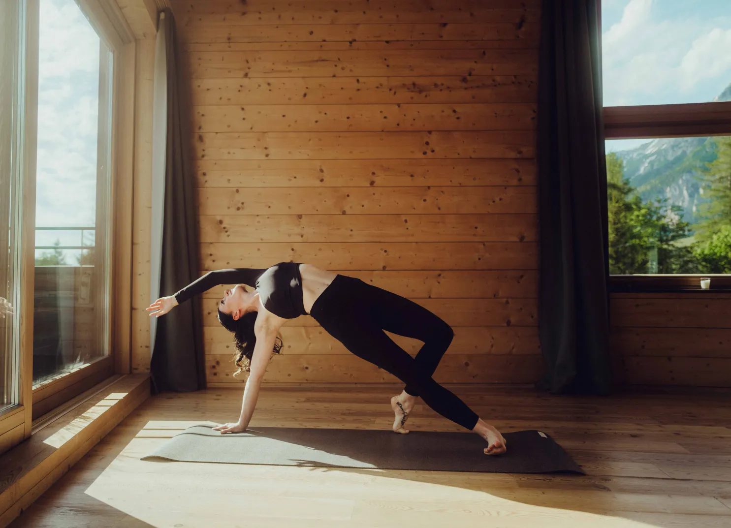 Woman in yoga pose in a wooden room with windows and nature view