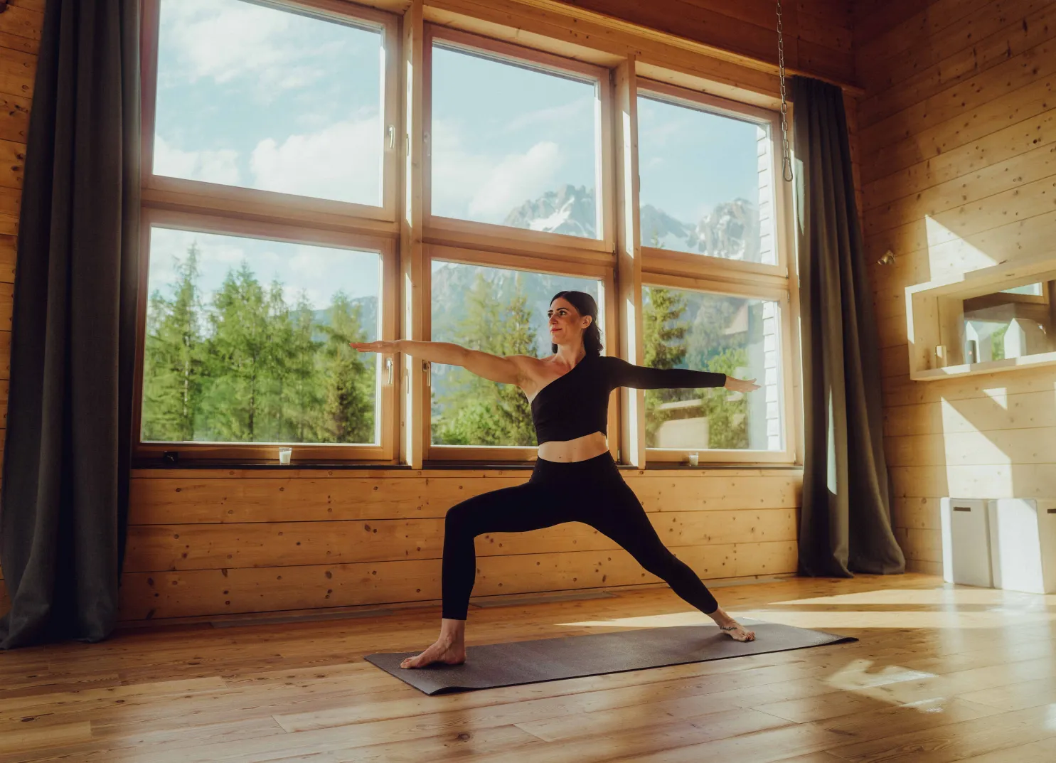 Woman practicing yoga in a wooden room with large windows and mountain view