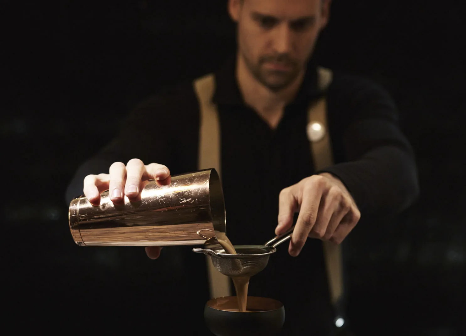Bartender pouring liquid from a copper shaker into a glass