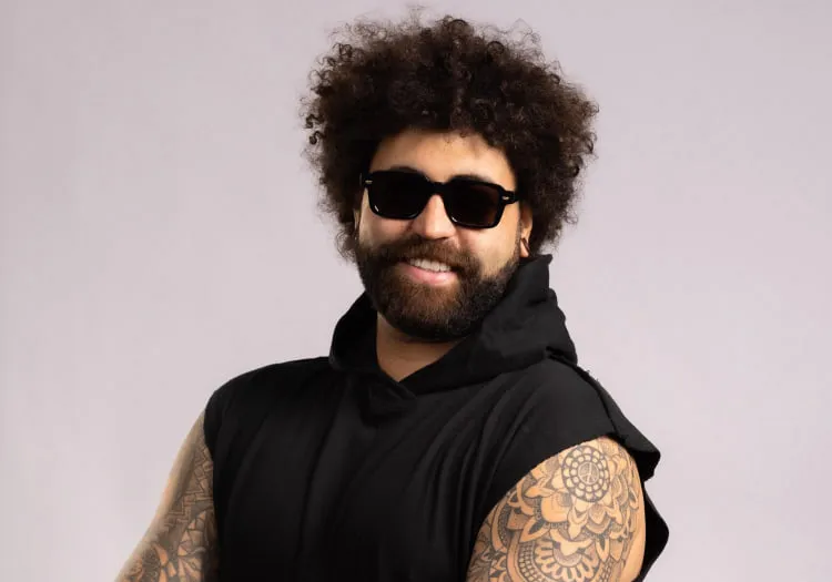 Man with curly hair and tattoos, wearing sunglasses and a sleeveless top
