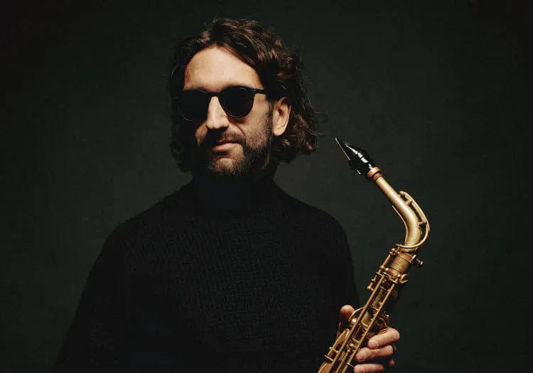 Man wearing sunglasses holding a saxophone