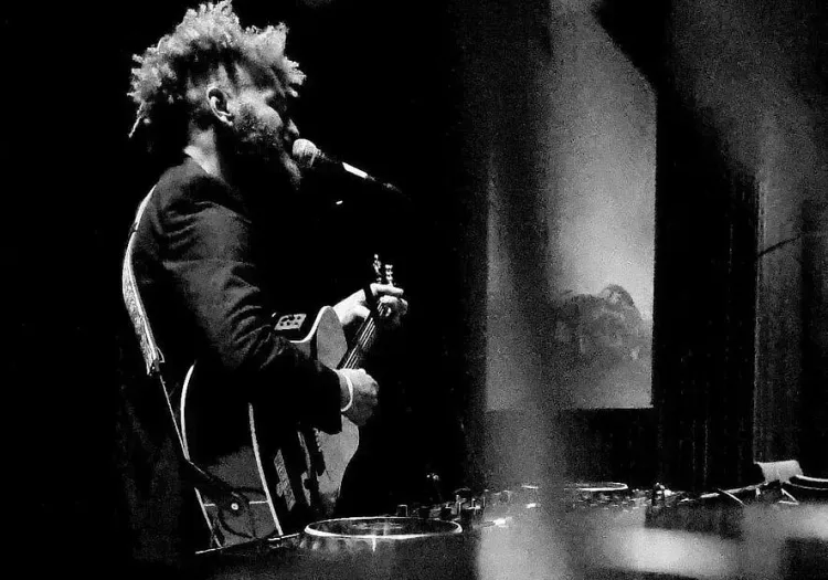 Man playing guitar and singing on stage in dim light