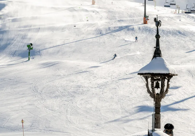 Snow-covered ski area with skiers and lifts, wooden hotel in the foreground