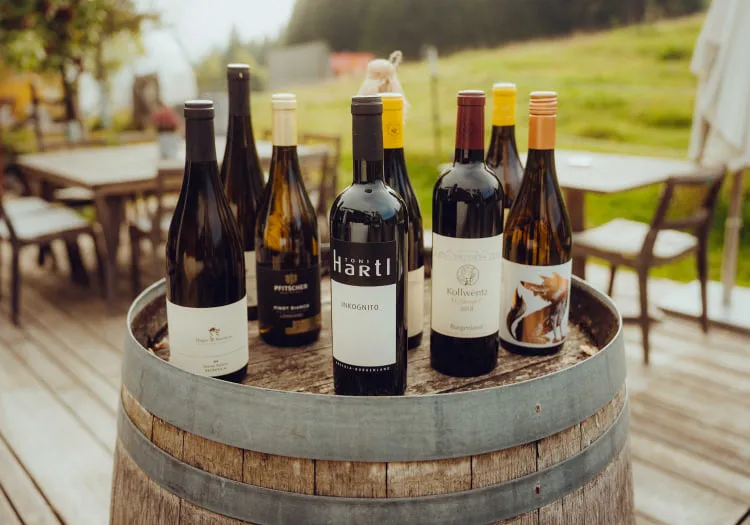 Wine bottles on a wooden barrel outdoors, with a grassy background.