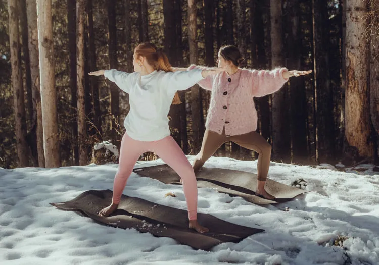 Two women practicing yoga on mats in snowy forest