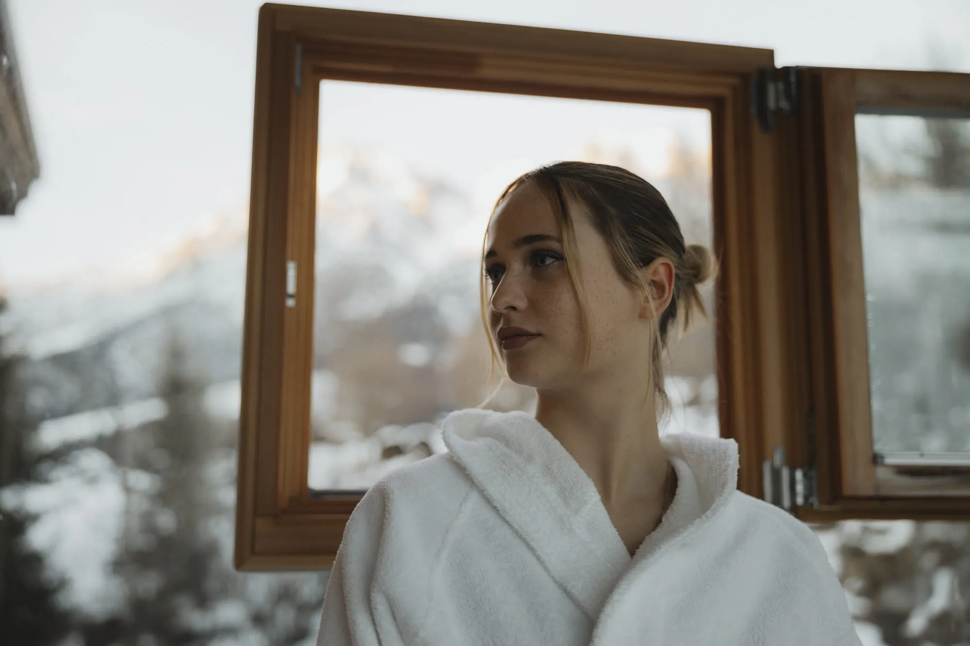 Frau in Bademantel, Blick aus Fenster im Holzhotel Forsthofalm, Winterlandschaft