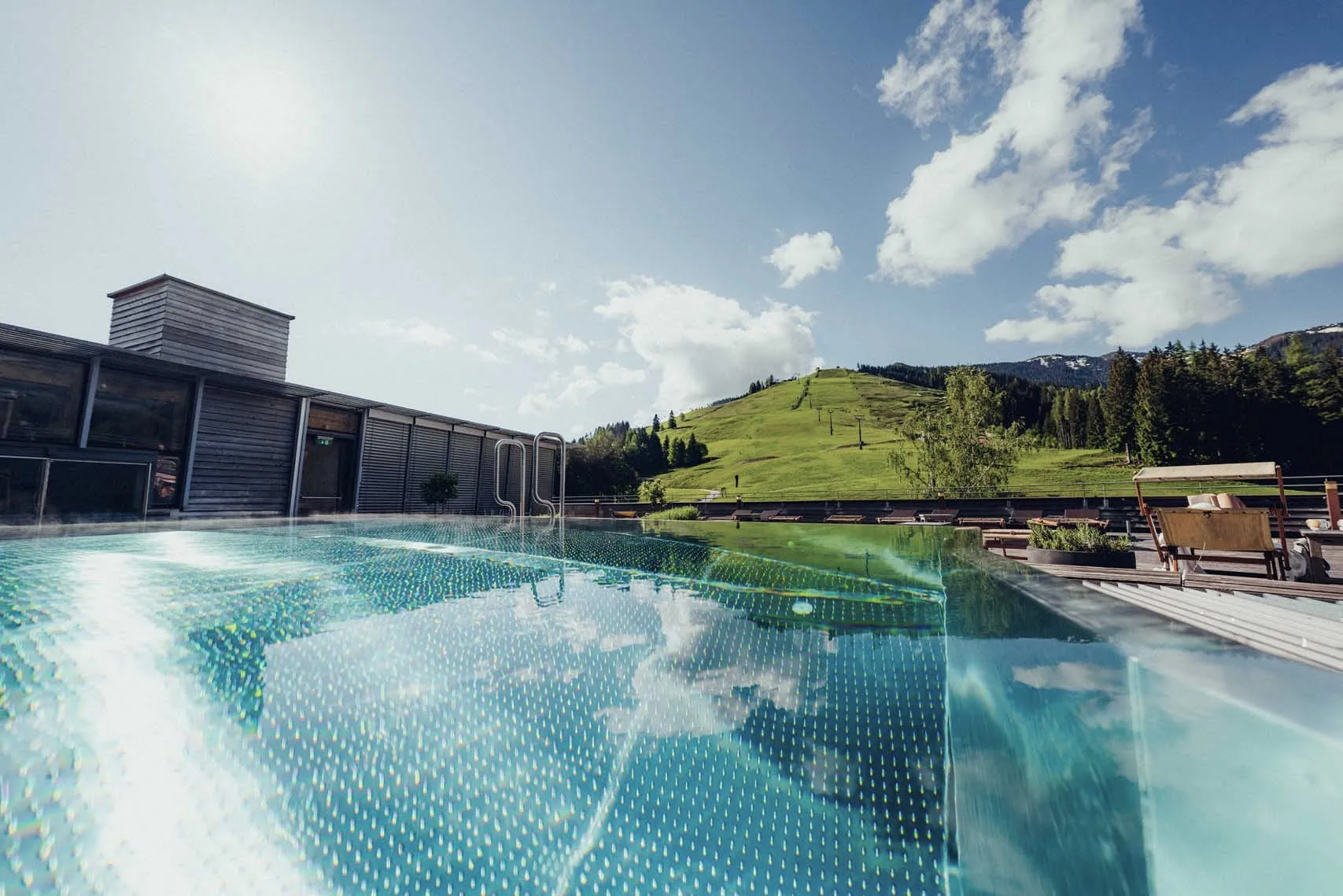 Moderner Pool mit Blick auf grüne Hügel und Wolken am Himmel.