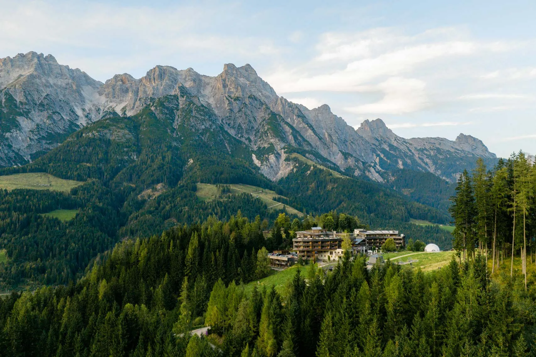Berglandschaft mit Hotel und Wälder im Vordergrund.