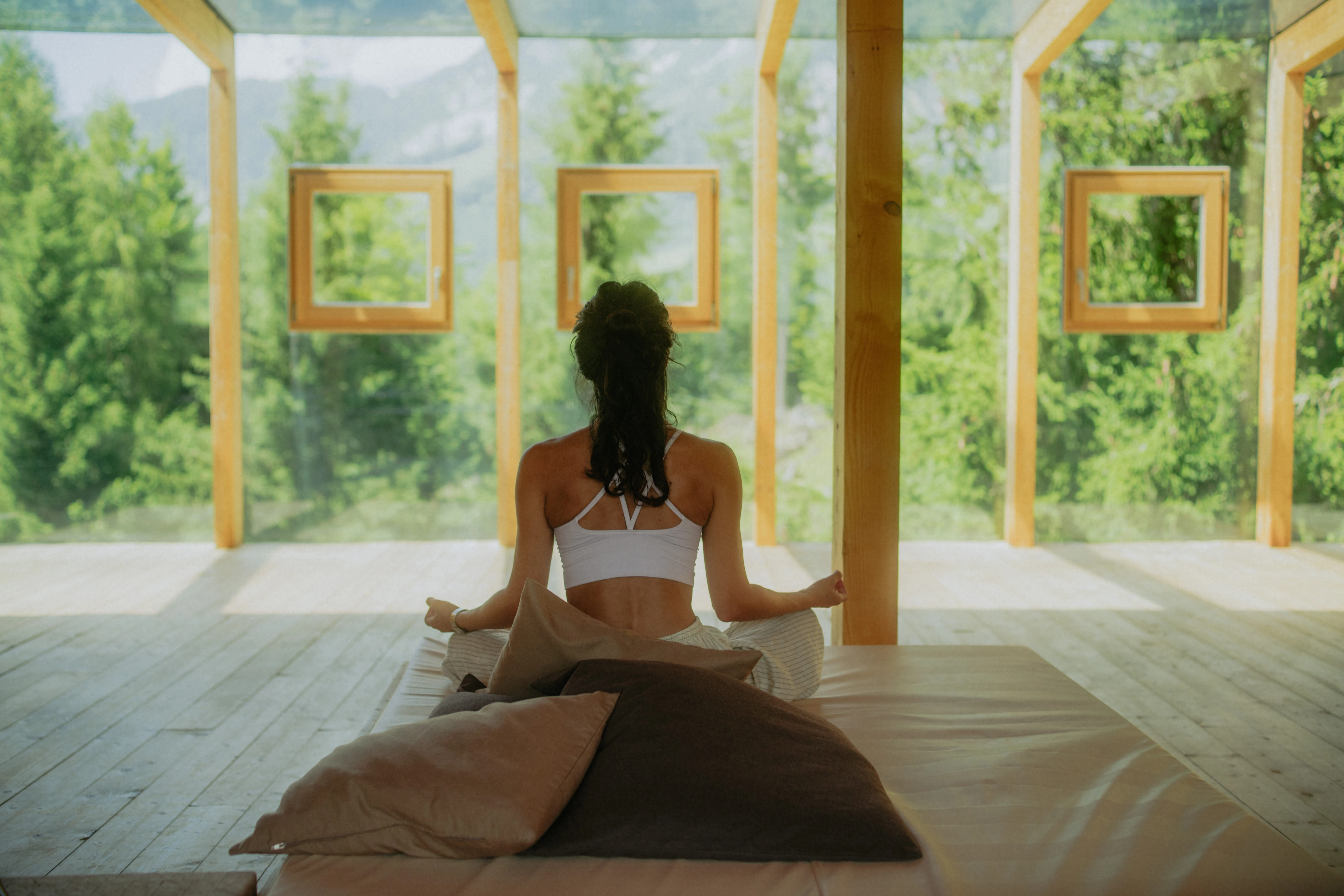 Frau sitzt meditierend in einem modernen Raum mit großen Fenstern und Blick ins Grüne