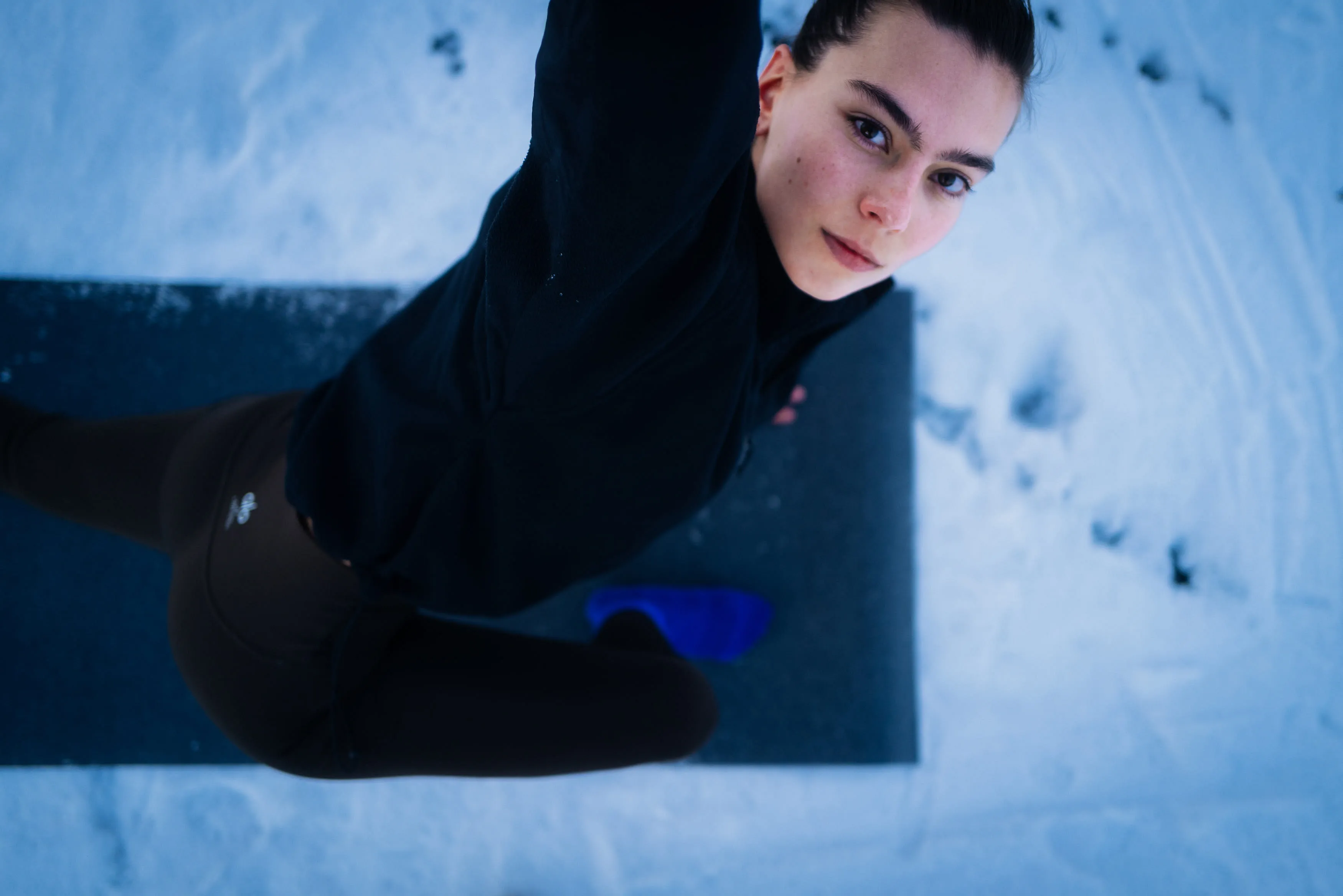 Person macht eine Yoga-Übung auf einer Matte in einer schneebedeckten Umgebung