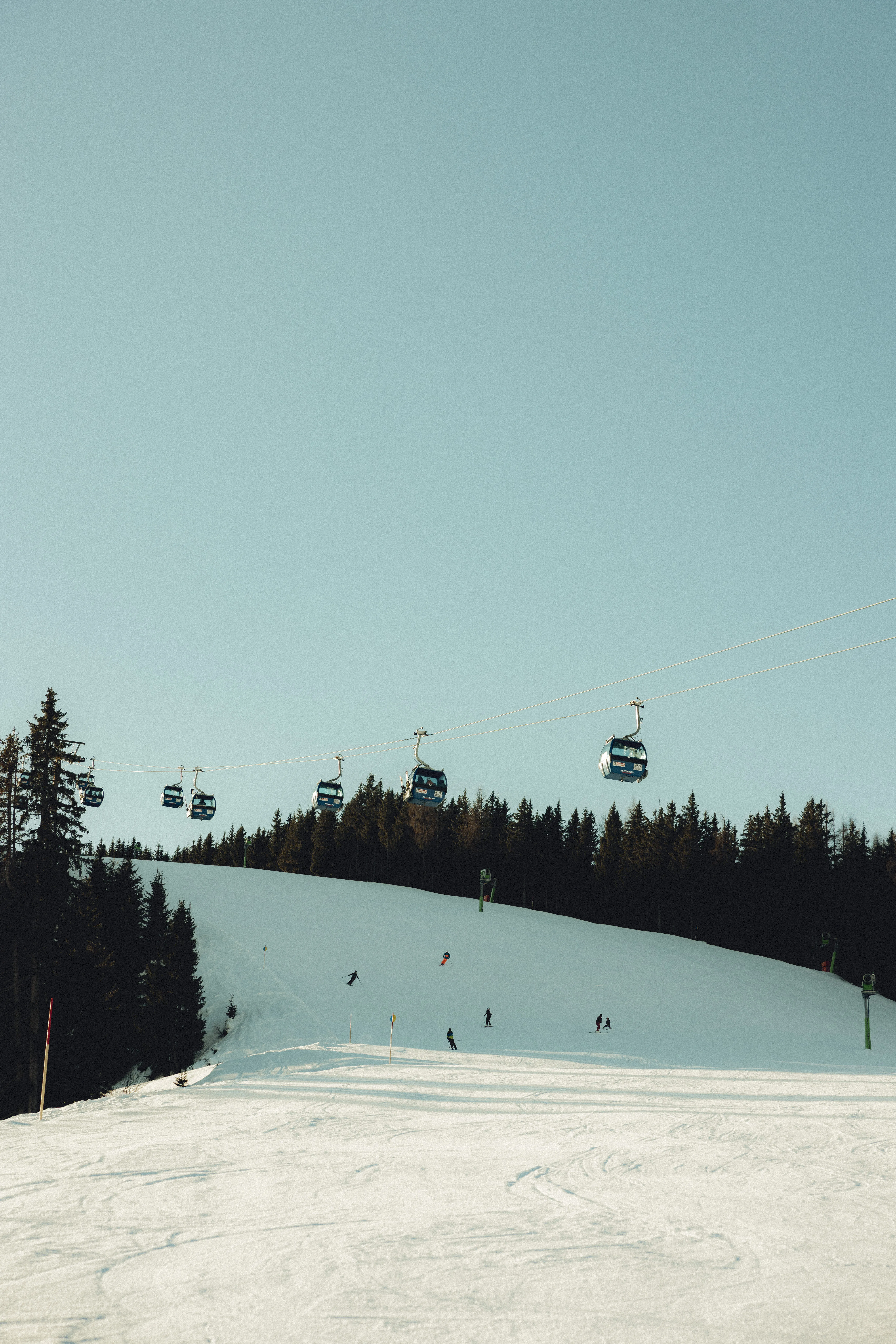 Skilifte über eine verschneite Piste mit Skifahrern im Vordergrund