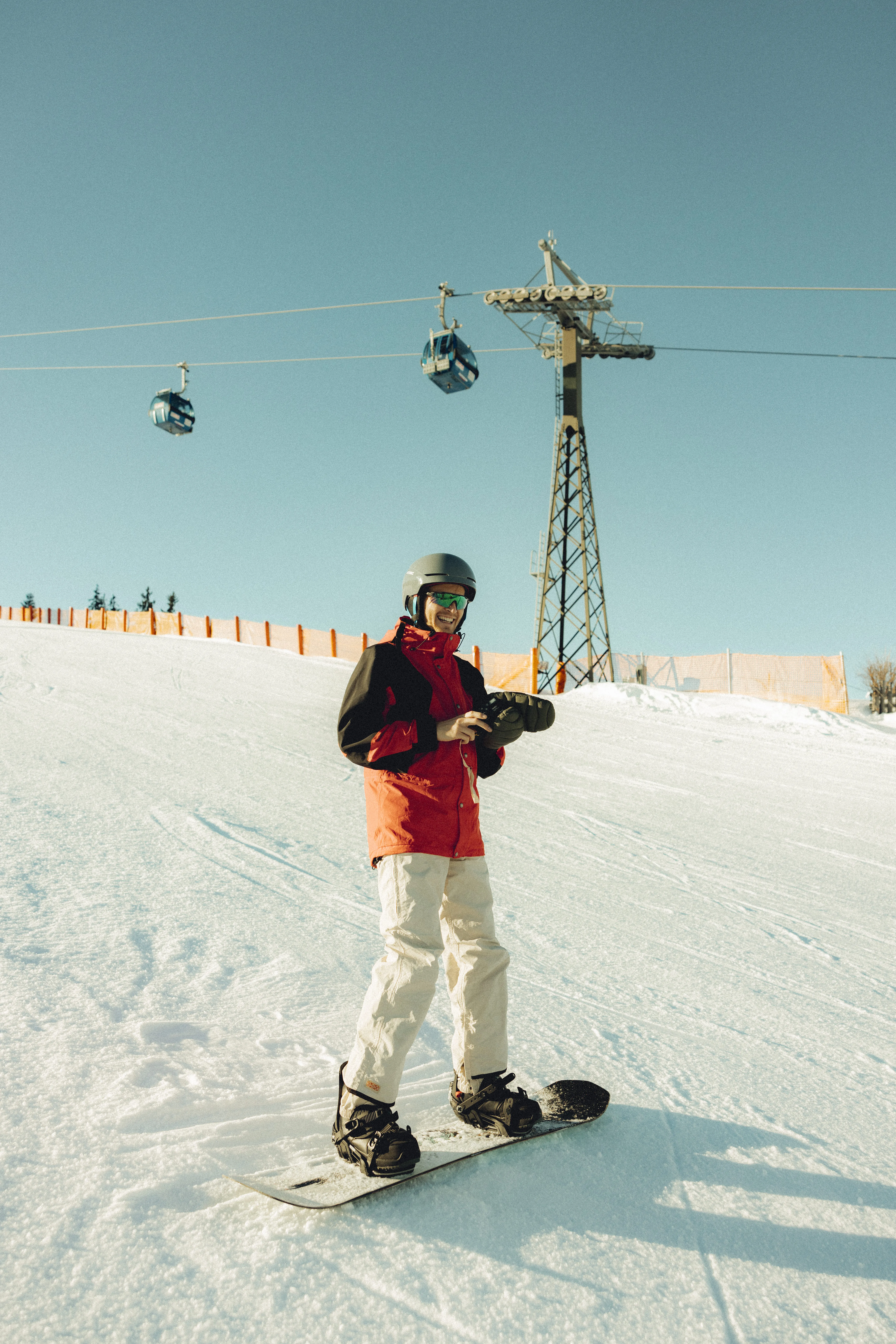 Ein Snowboarder steht auf der Piste bei der Forsthofalm, Seilbahnen im Hintergrund.