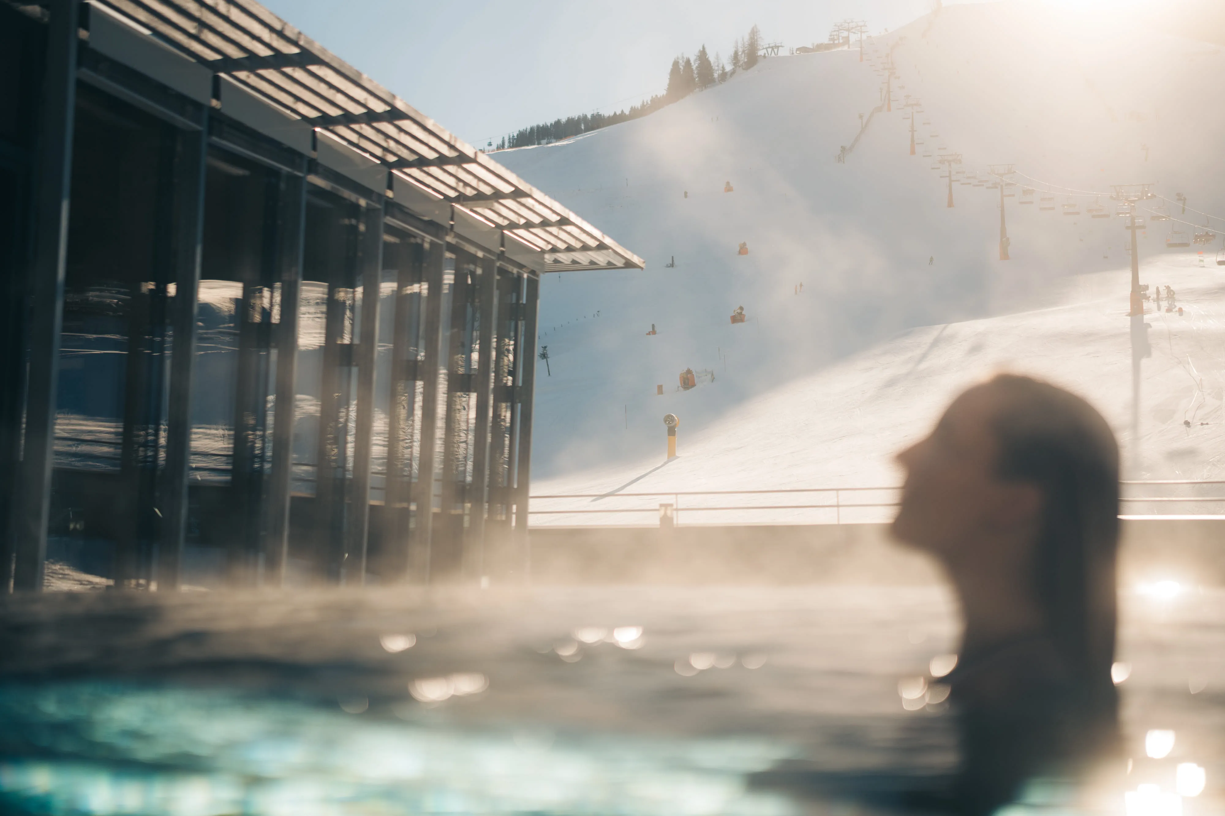 Frau im Pool mit Blick auf schneebedeckte Pisten und Skifahrer