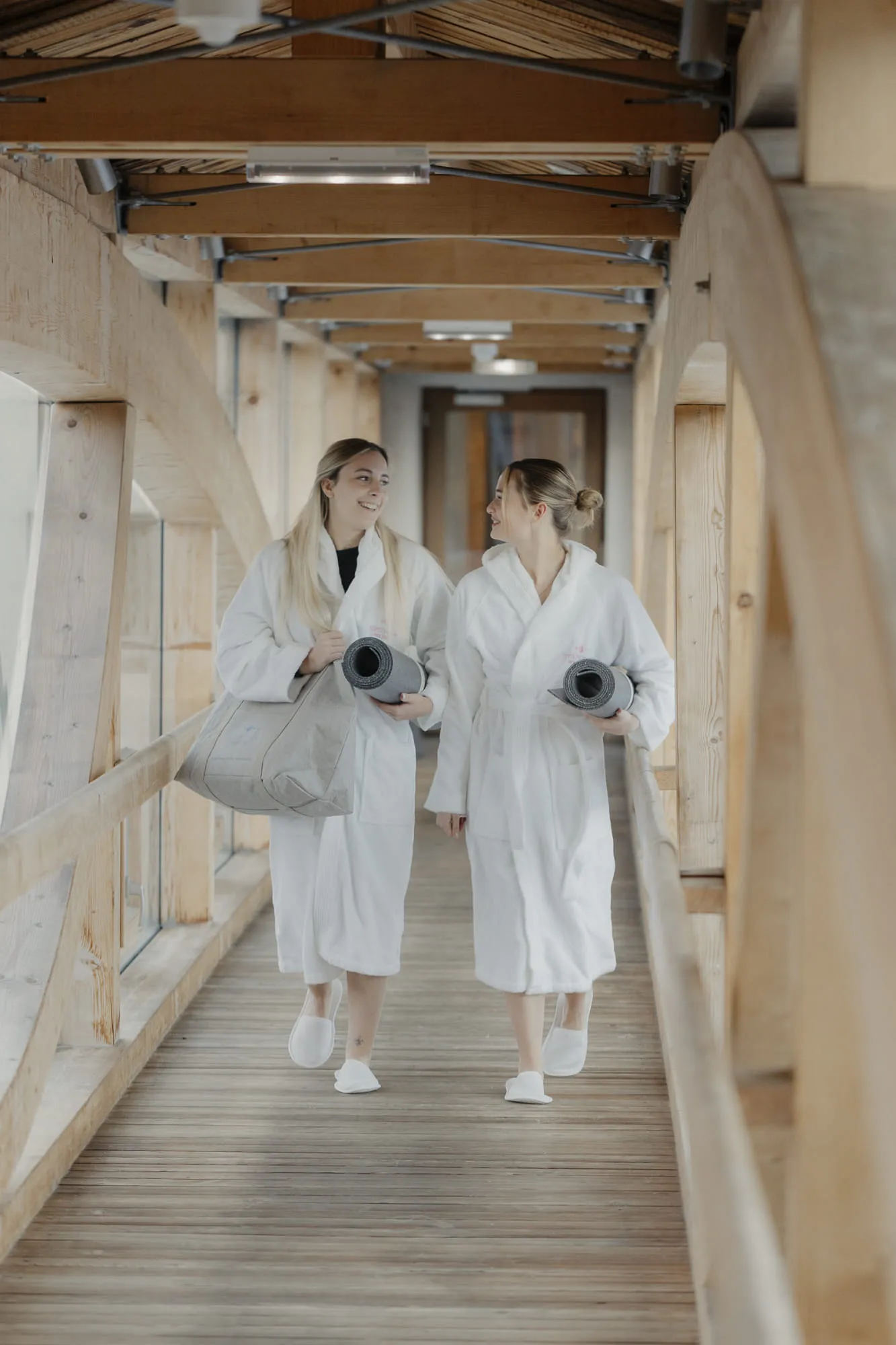 Two women in bathrobes walking through a wooden corridor in Holzhotel Forsthofalm.