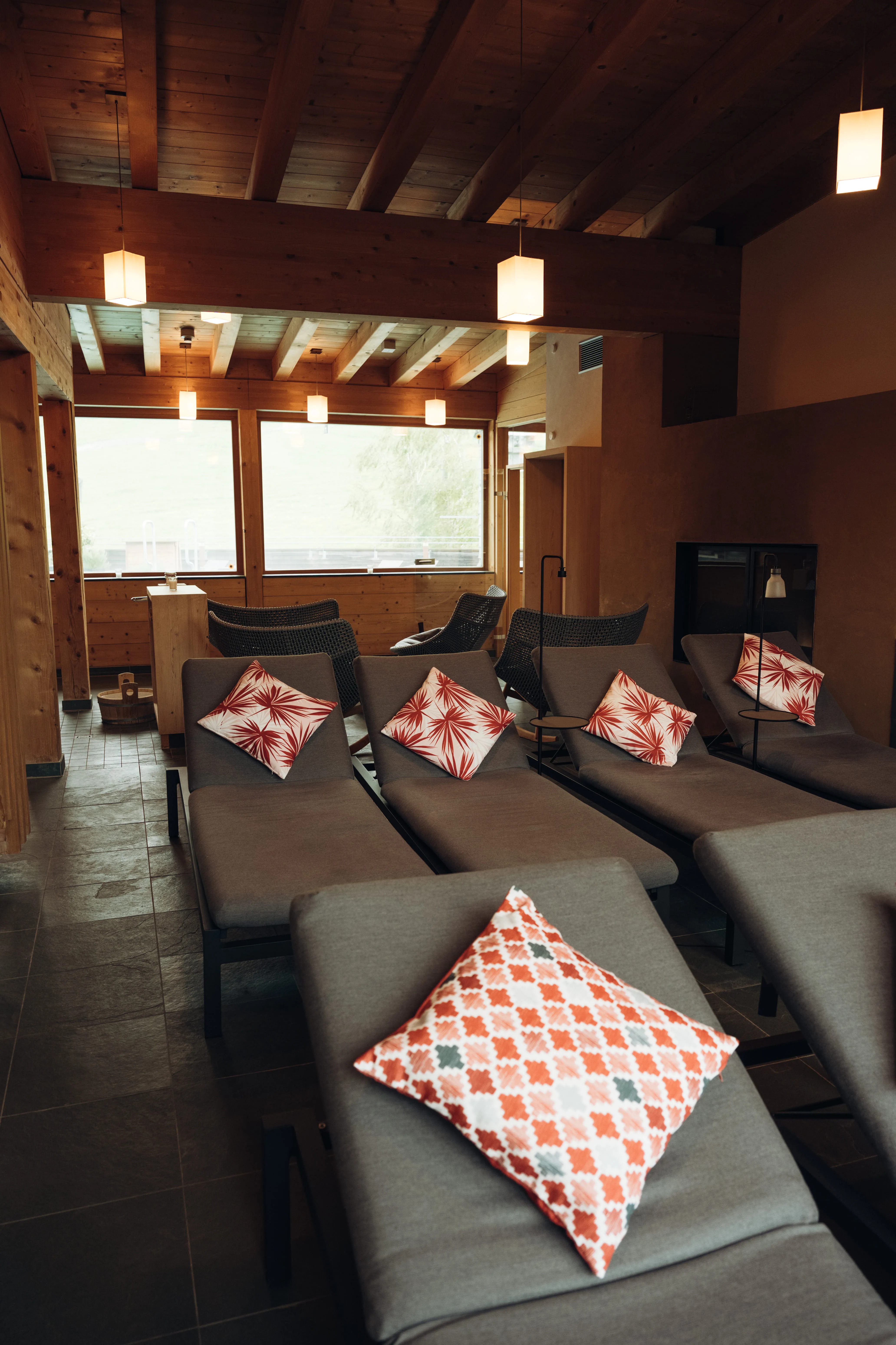 Lounge with lounge chairs and colorful pillows, wooden ceiling and windows.