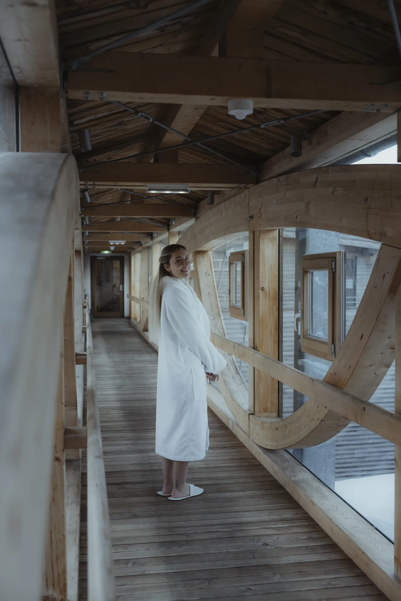 Woman in a bathrobe in the Holzhotel Forsthofalm, Leogang, on a wooden corridor.