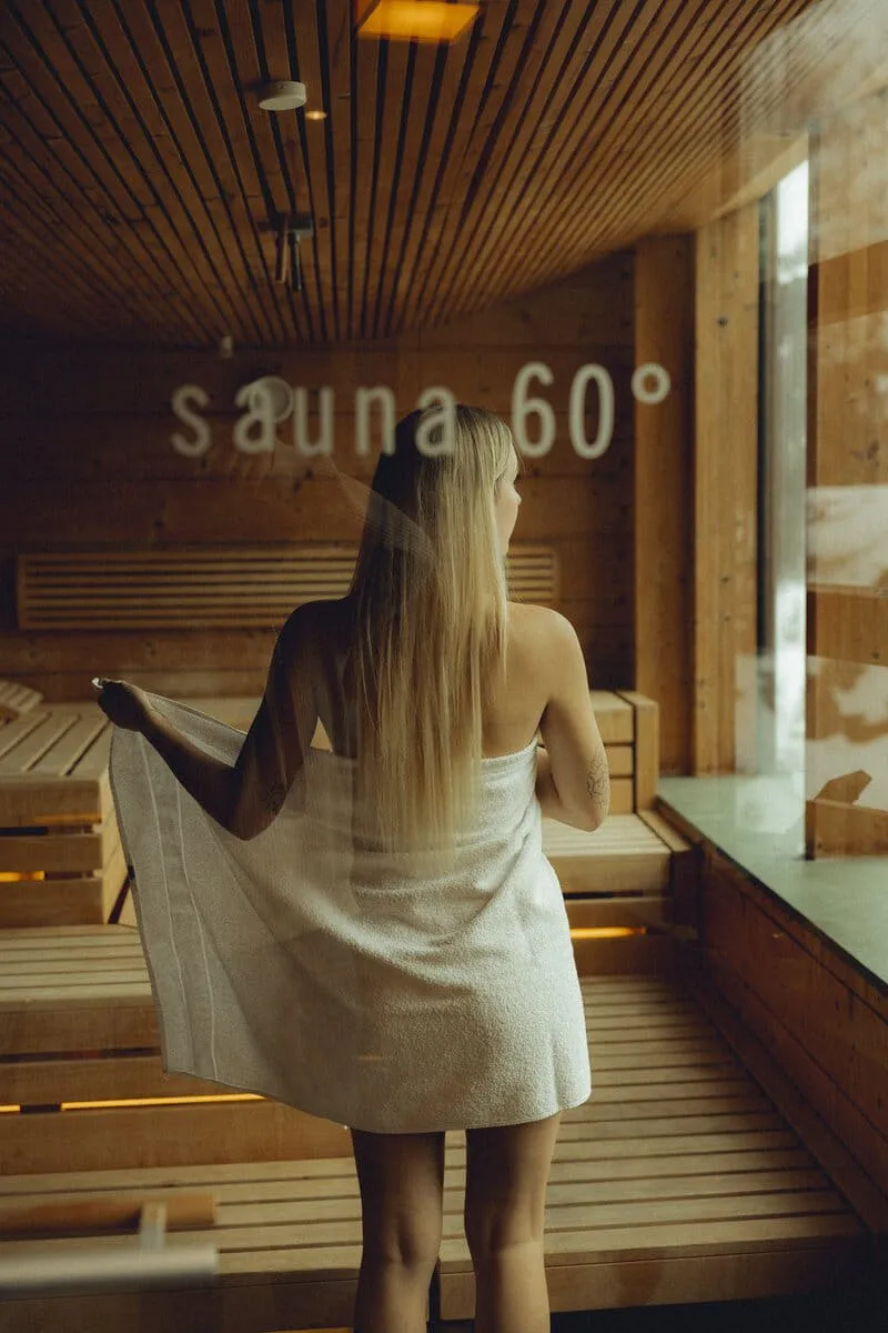 Woman with towel in a sauna, wooden interior and 60° sign.