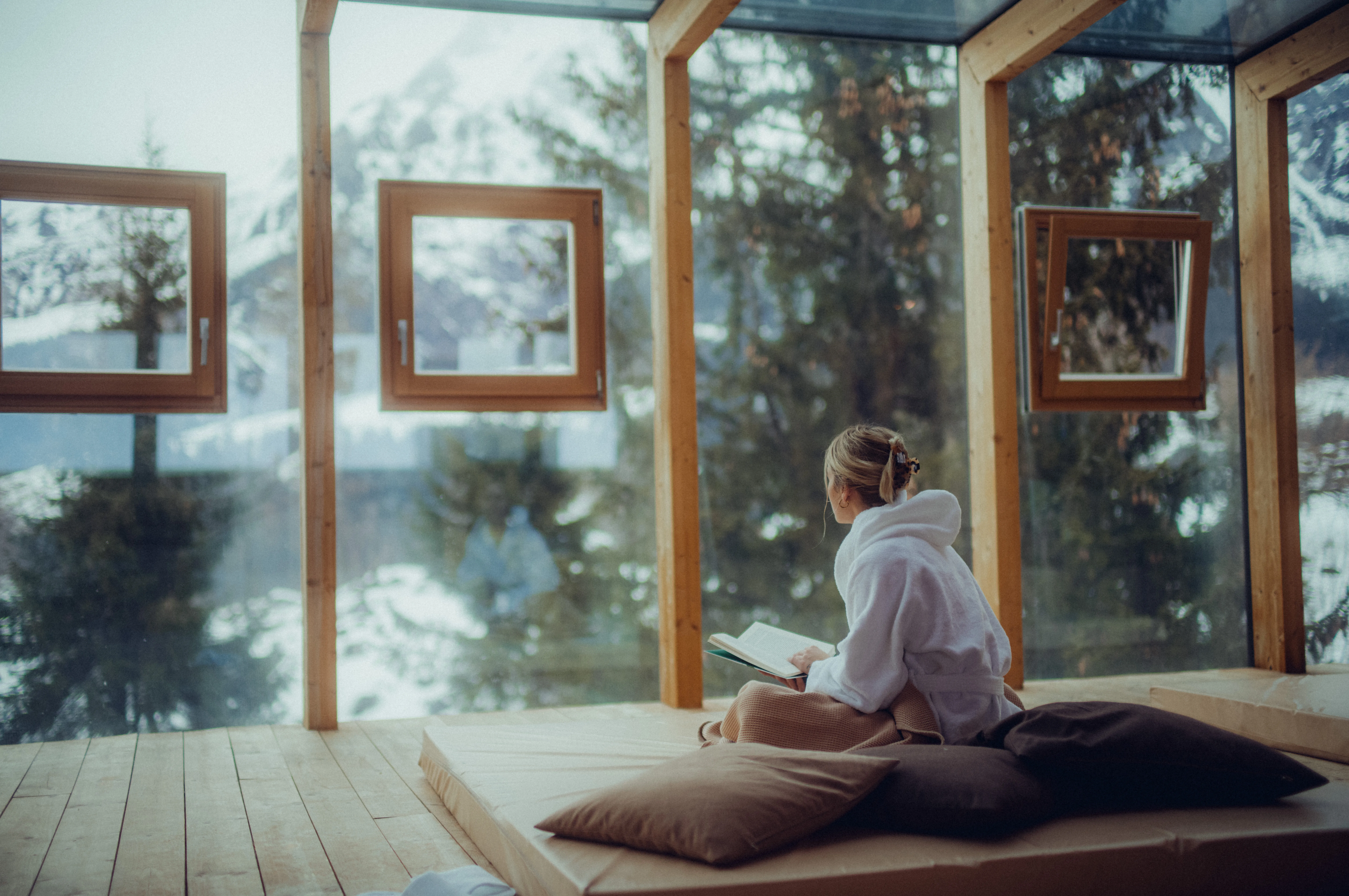 Person reading in a cozy space with large windows and mountain views