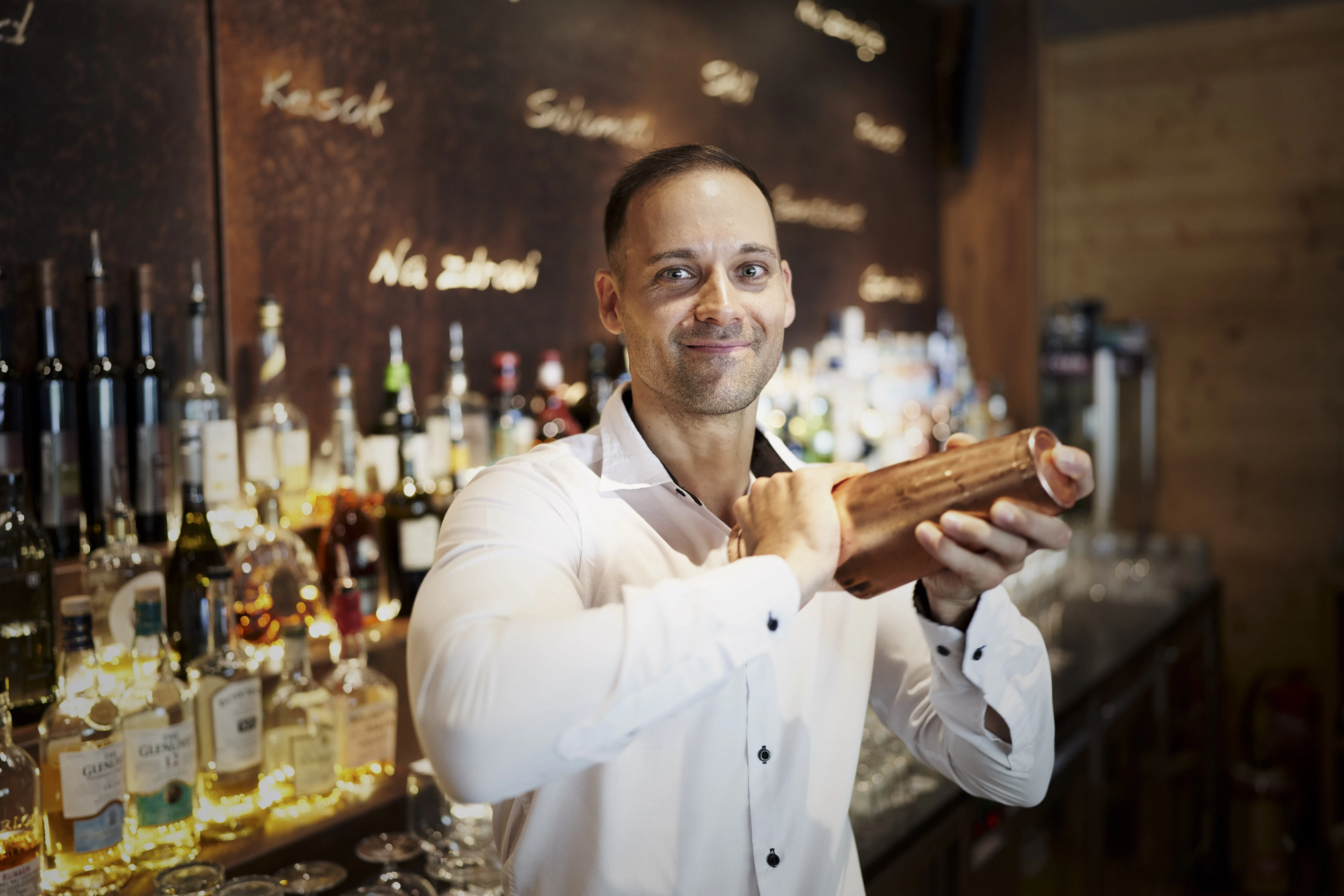 Man with shaker behind a bar with various spirits