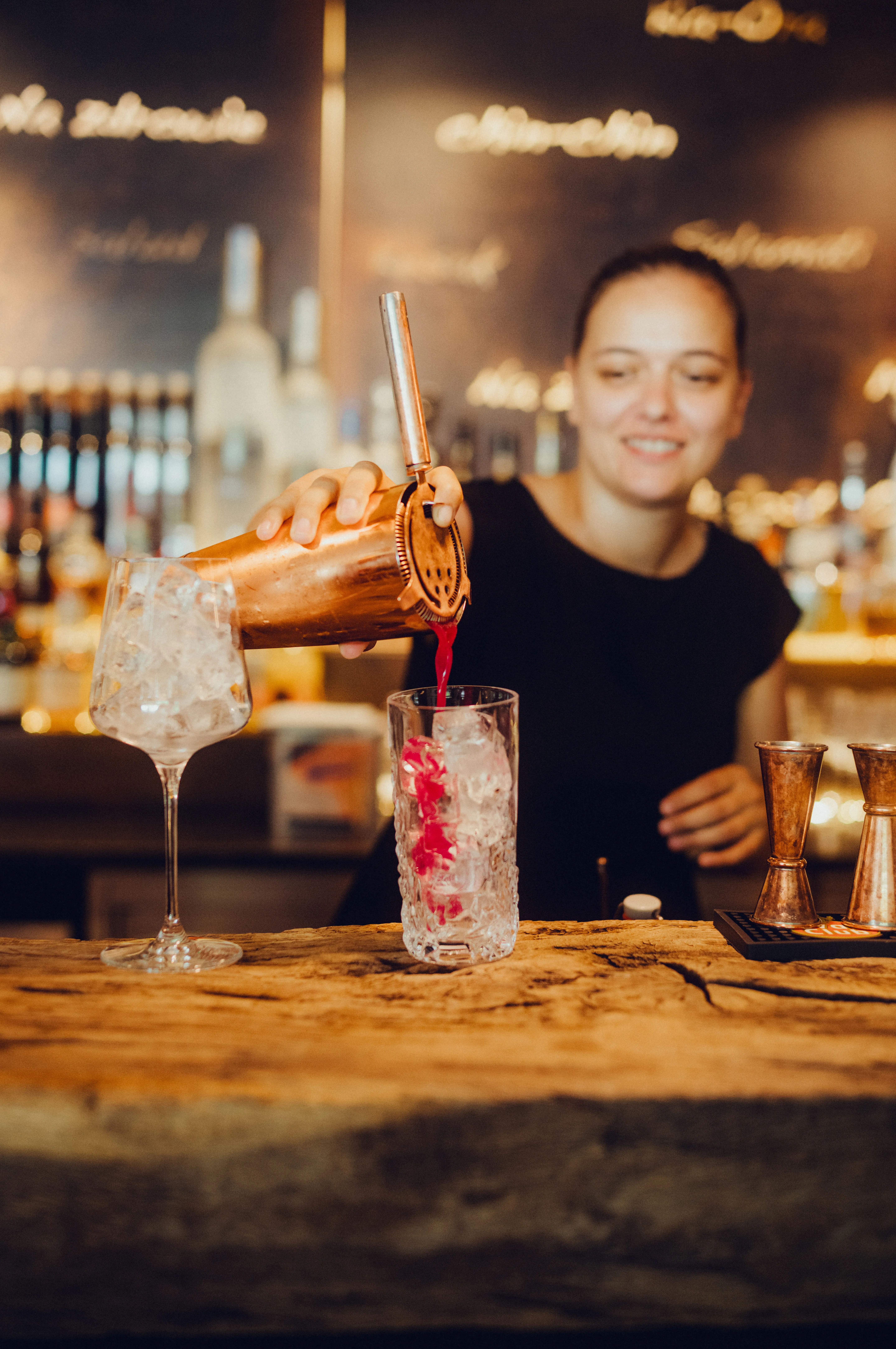 Bartender pouring a cocktail into a glass at a bar