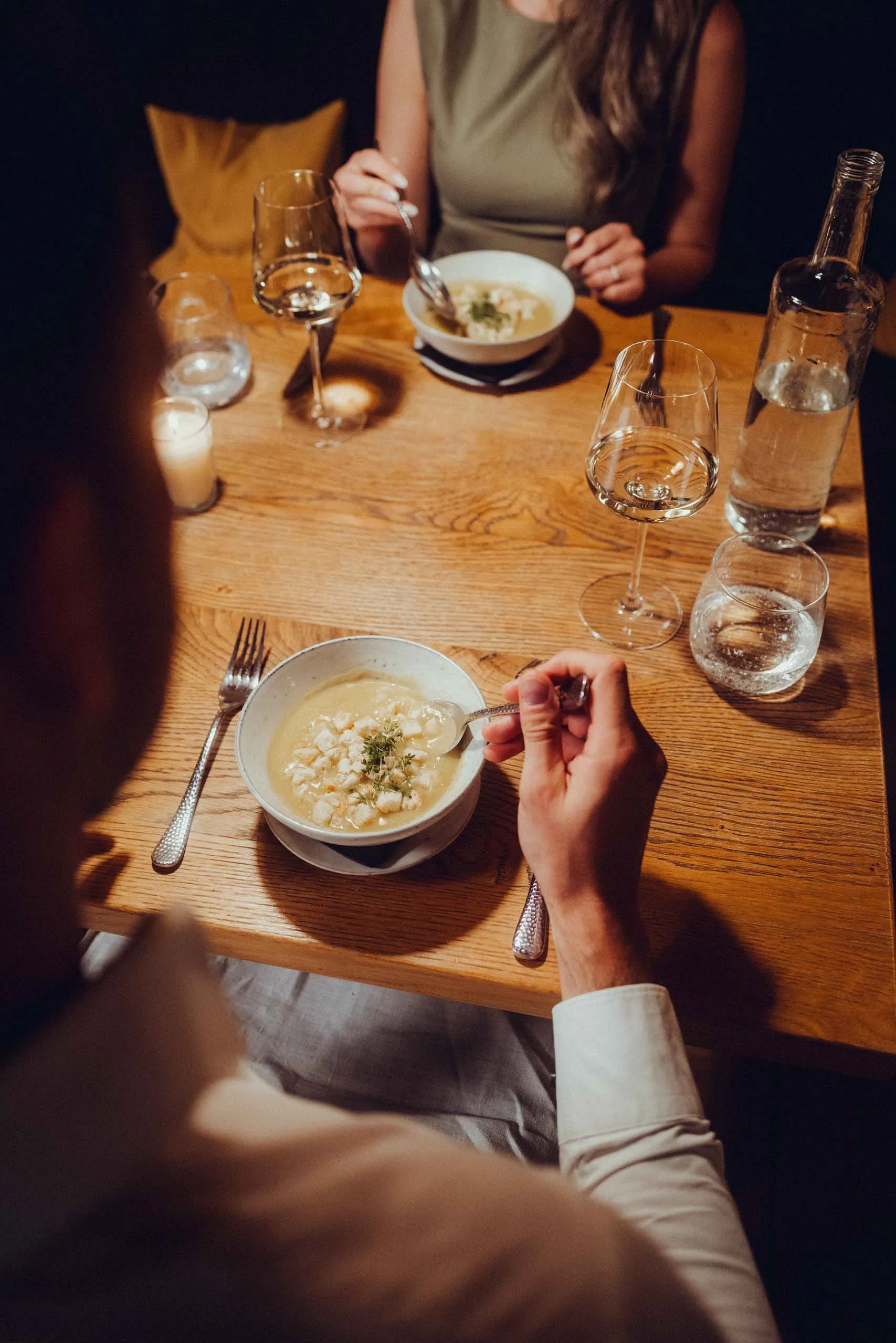 Table setting with one person eating soup and another in the background.
