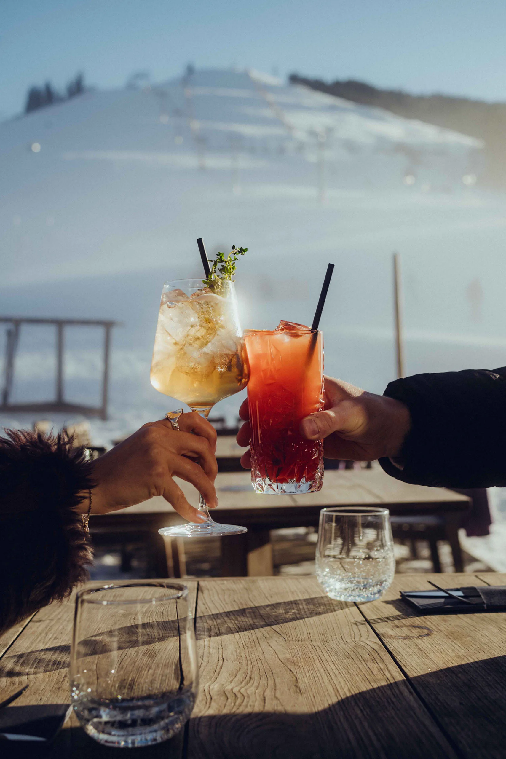 Two cocktails being toasted at a table in a snowy setting.
