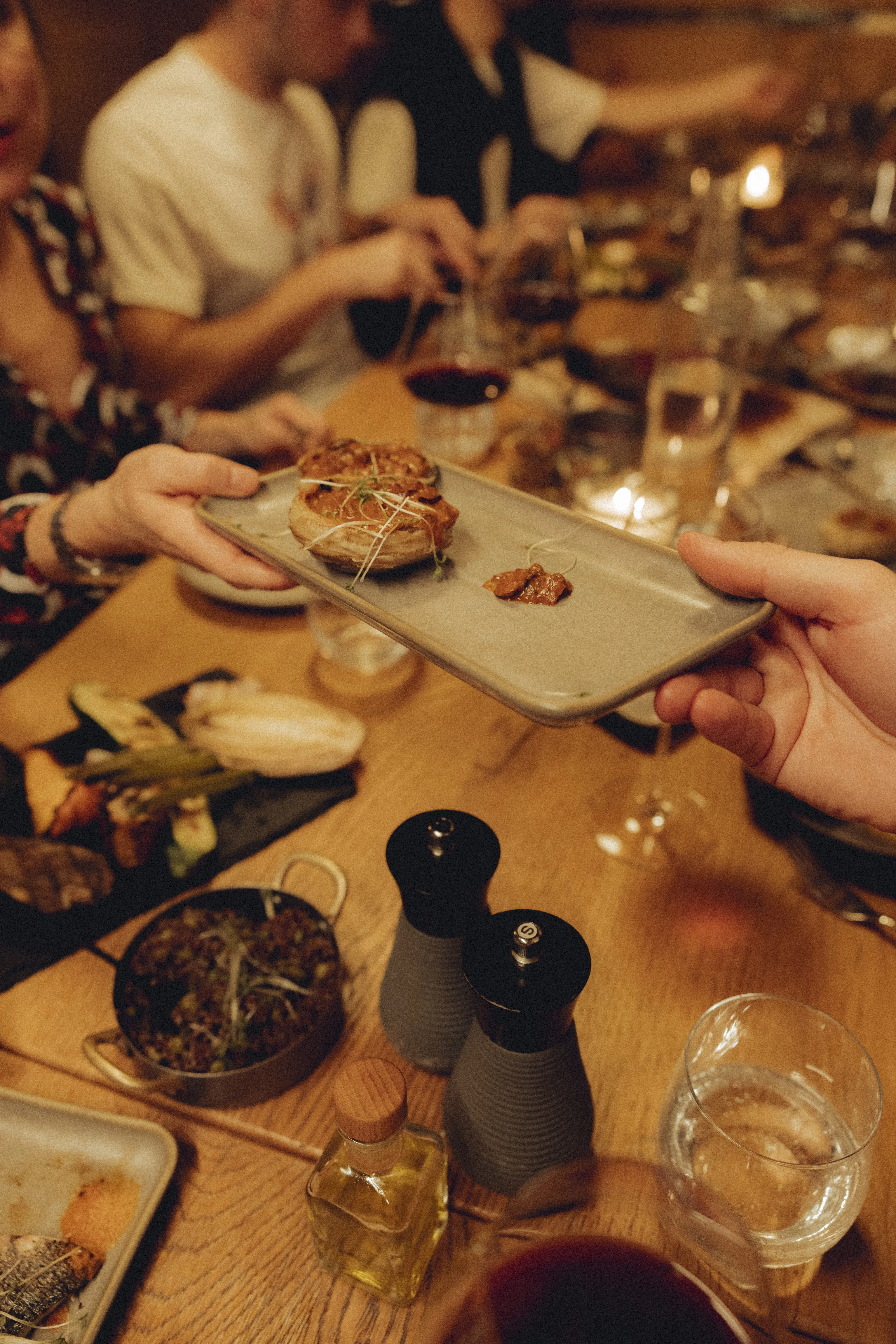 Dish is being handed over from one hand to another over a table with various food items.