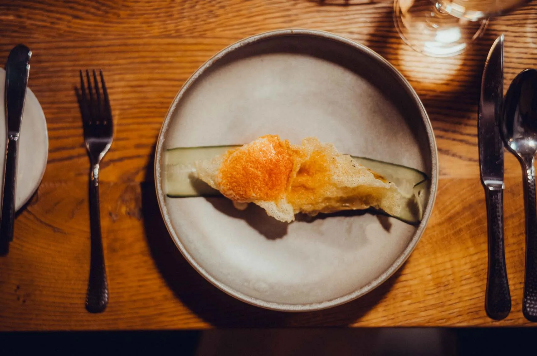 A plate with a dish on a wooden table, cutlery on both sides.