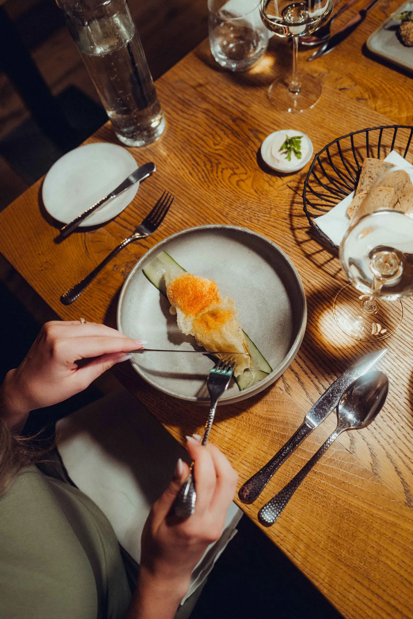 Someone is eating a dish on a plate, surrounded by glasses and cutlery.