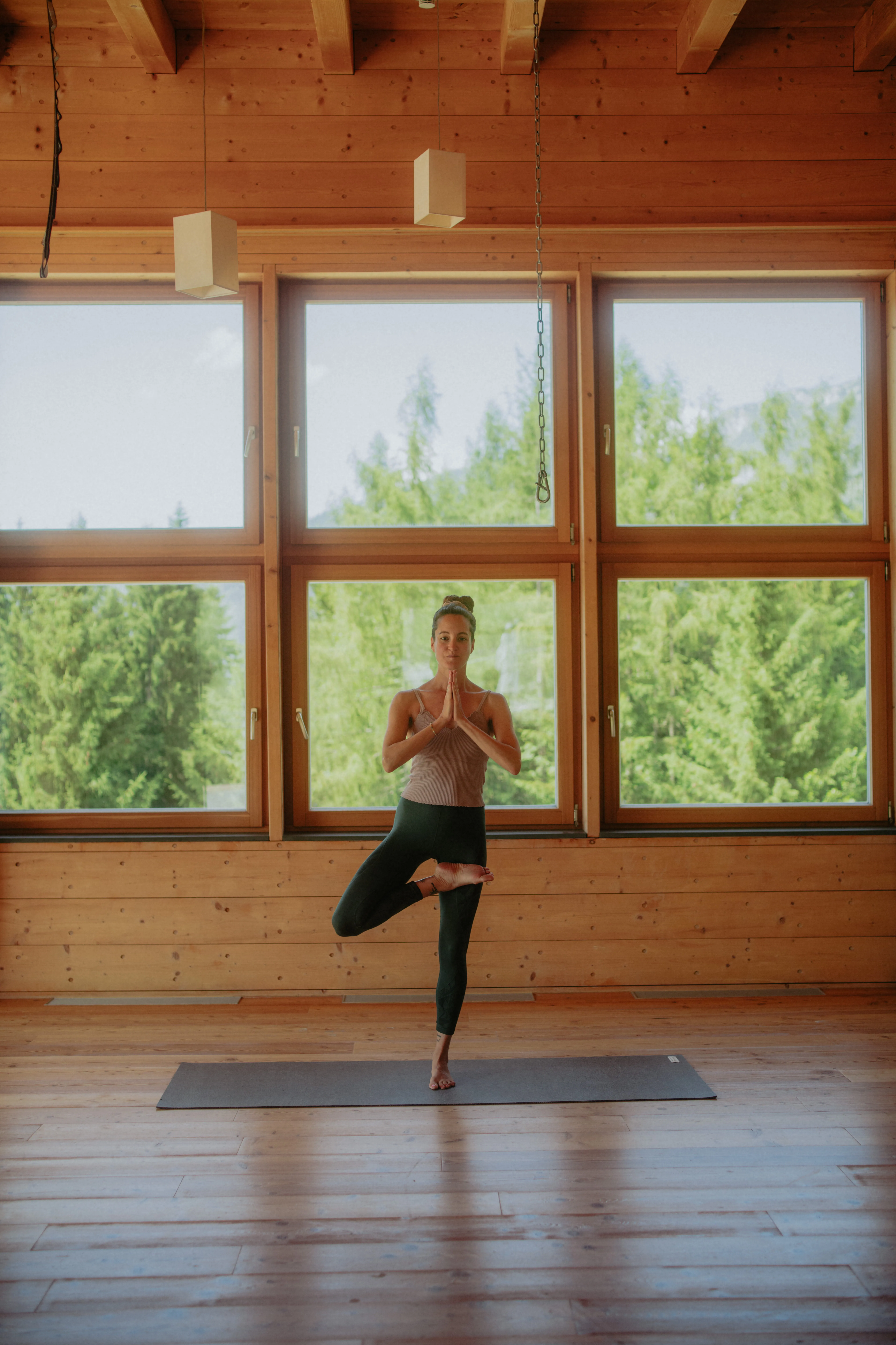 Person practicing yoga in tree pose inside a wooden room with large windows