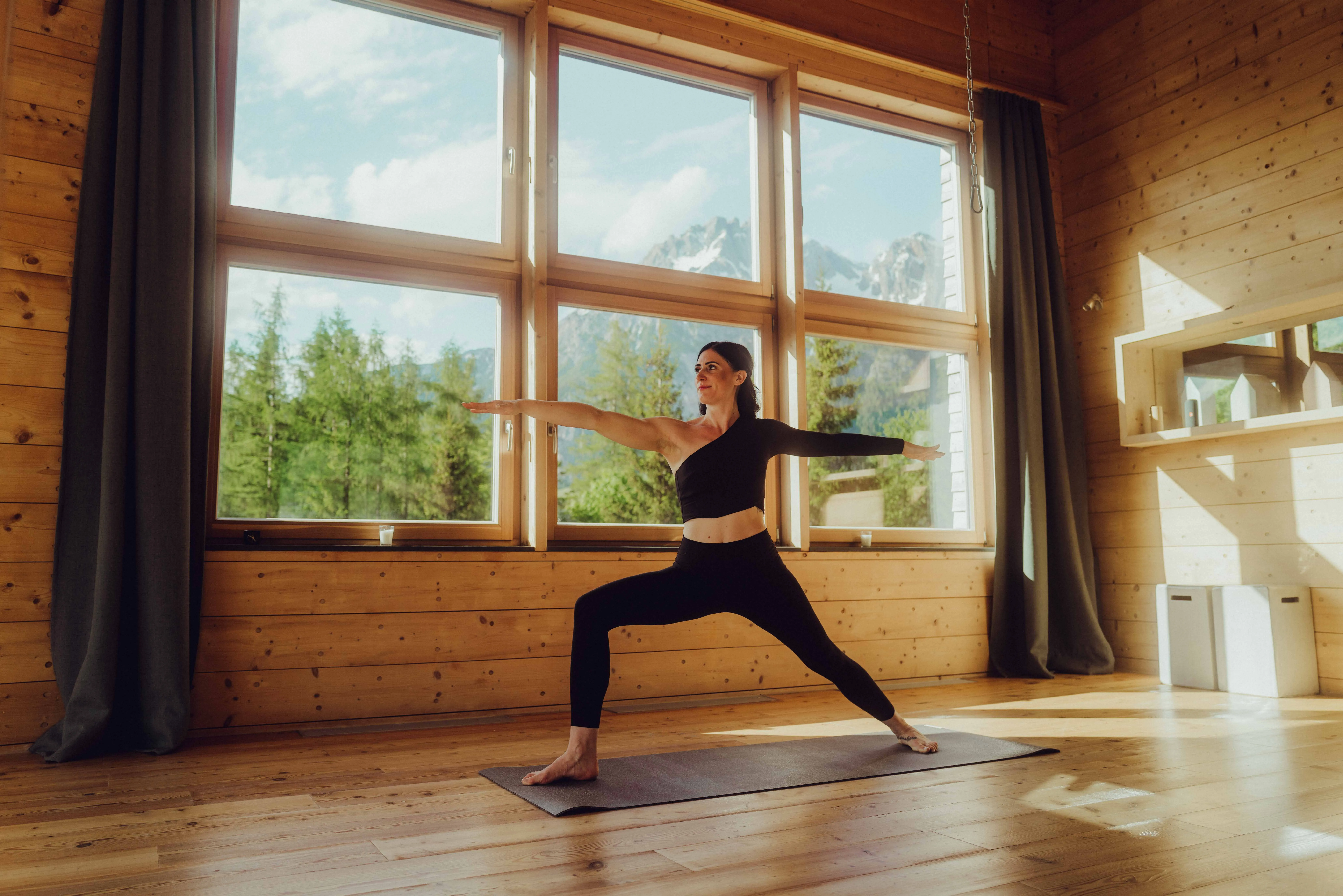Woman practicing yoga in a wooden room with windows and mountain views