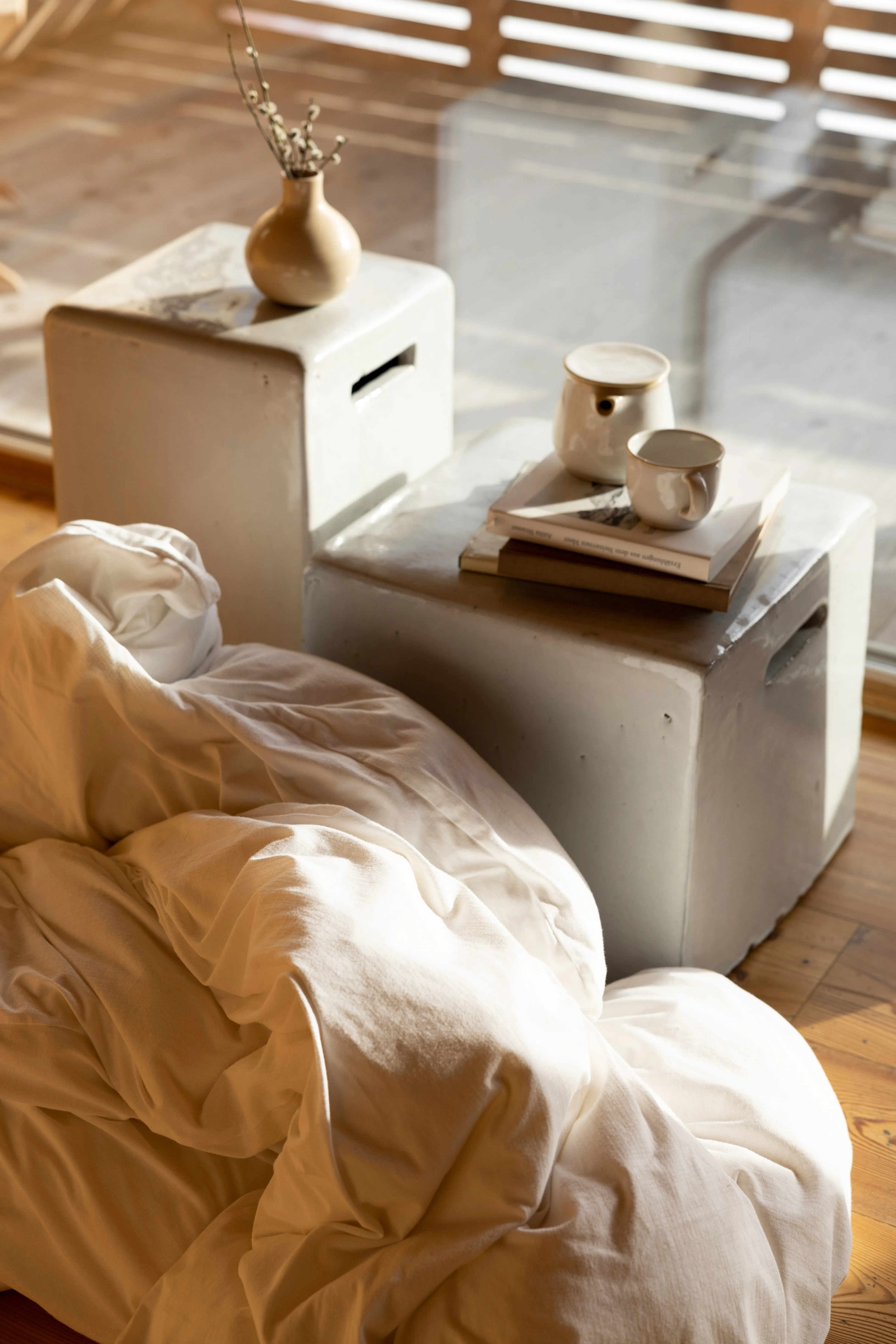 Cozy white bedding draped over a small table with a vase and cups.