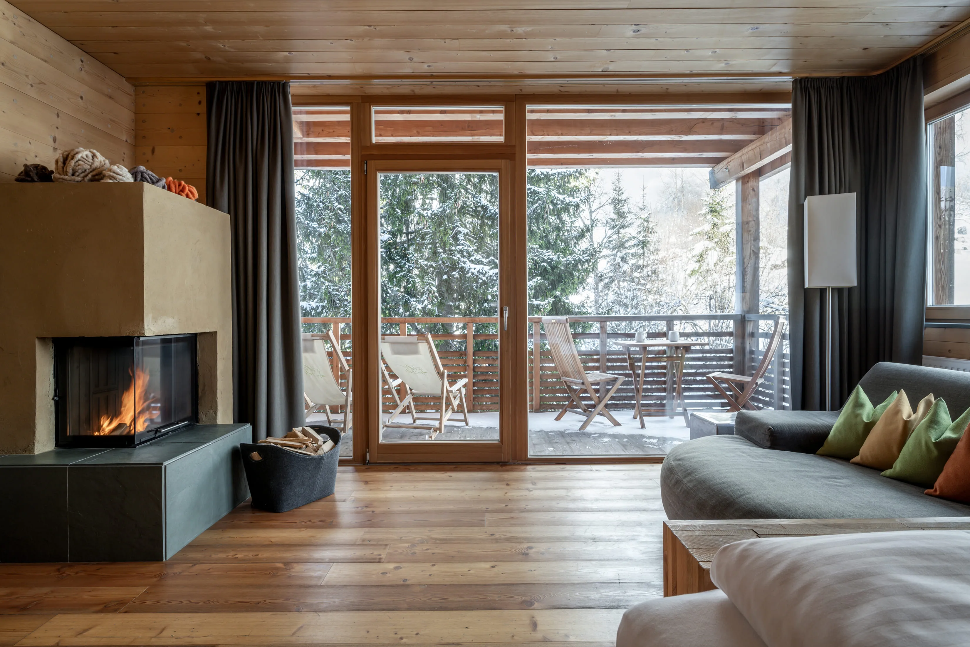 Cozy living space with fireplace and view of the balcony at Holzhotel Forsthofalm.