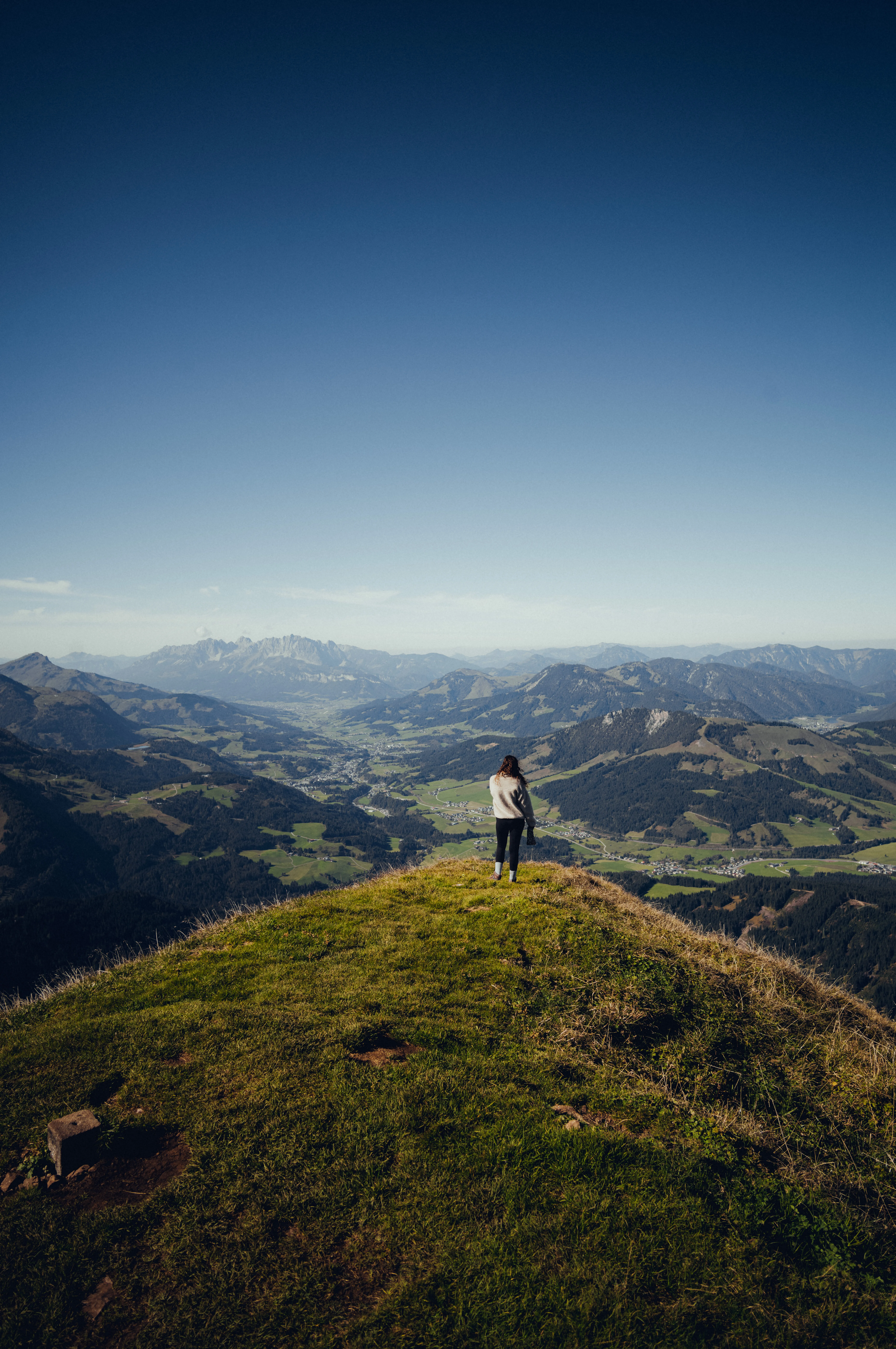 Eine Person steht auf einem Hügel mit Blick auf das Tal und die Berge.